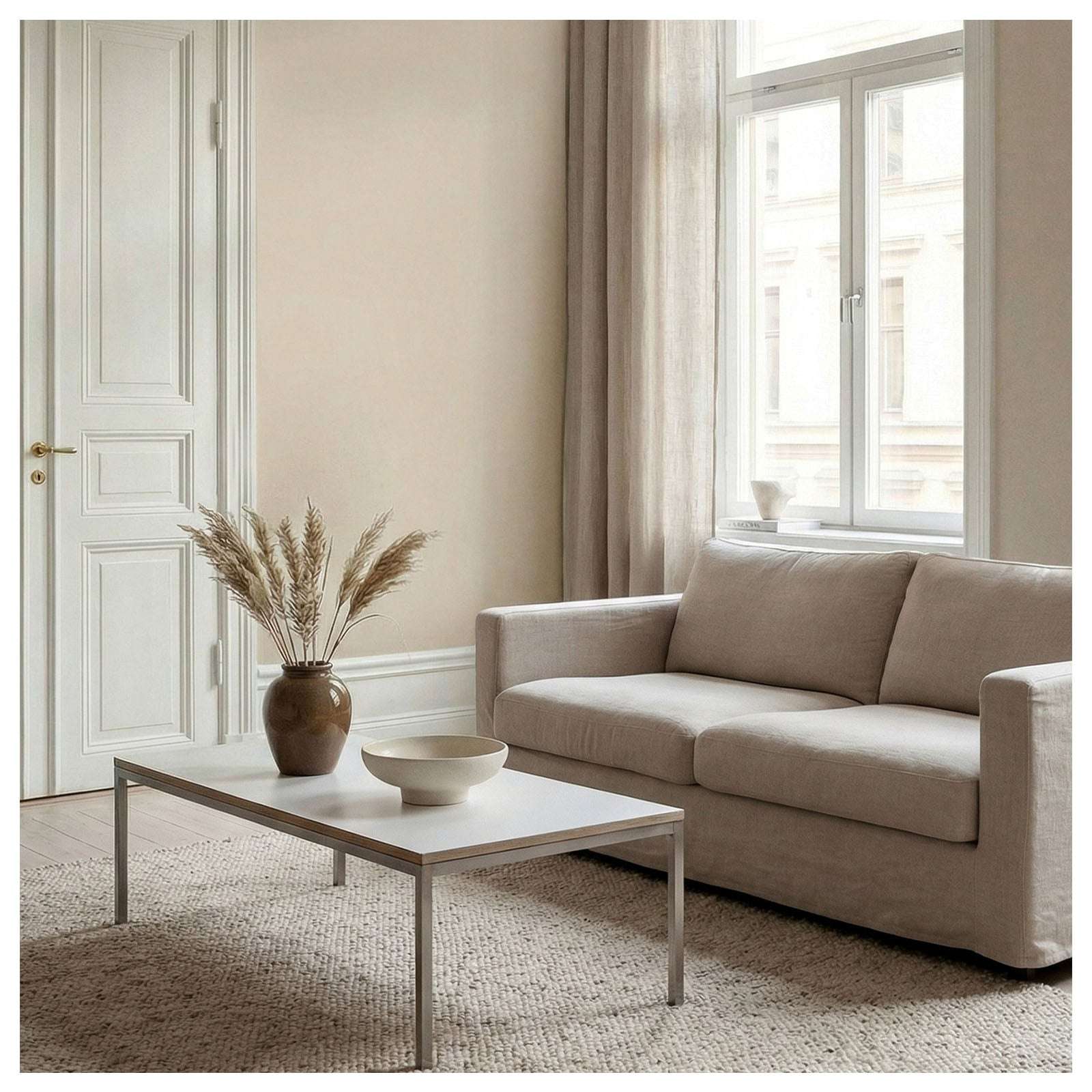 En stue med beige sofa og teppe. Veggene er malt i fargen Sand, en myk beige nyanse.