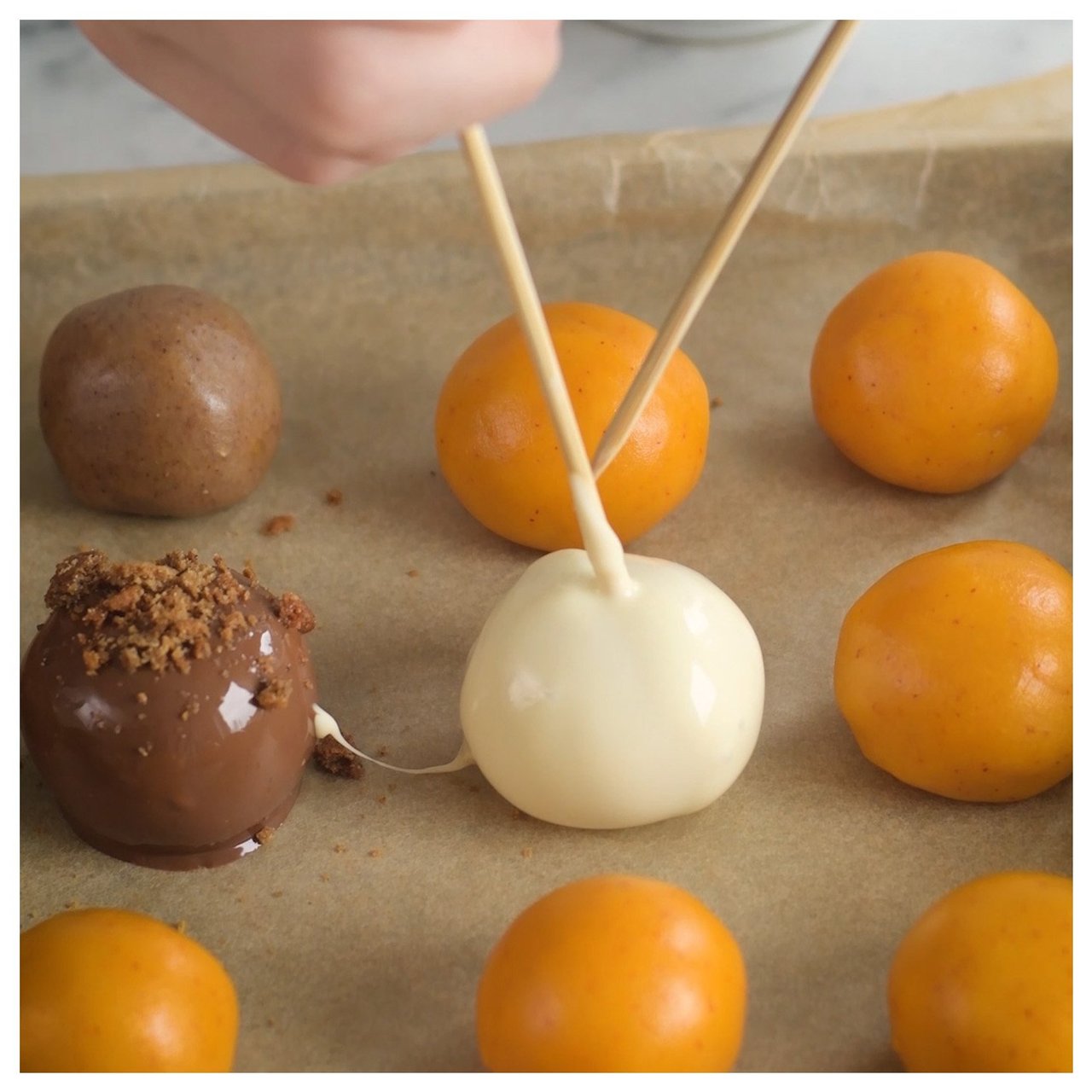 Käsi kastaa piparkakkupallon sulatettuun suklaaseen, ja useita palloja on leivinpellillä.