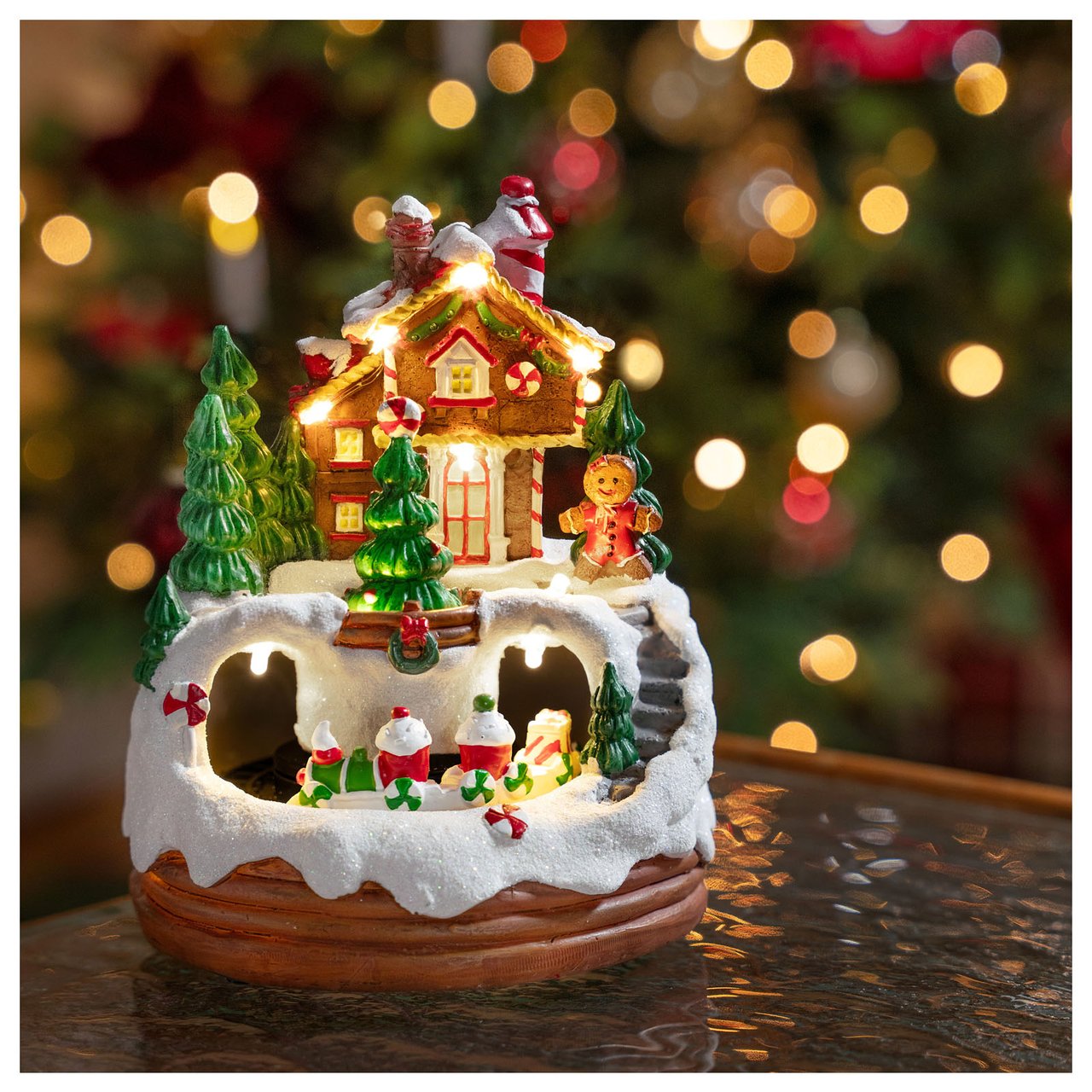 Lysande julby med pepparkaksgubbe, pepparkakshus, granar och ett tåg som kör genom snötäckt landskap.