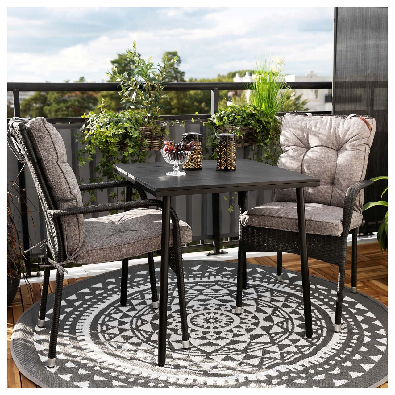 Zwei Stühle und ein Tisch auf einem Teil des Balkons mit einem runden Bastteppich als Unterlage.