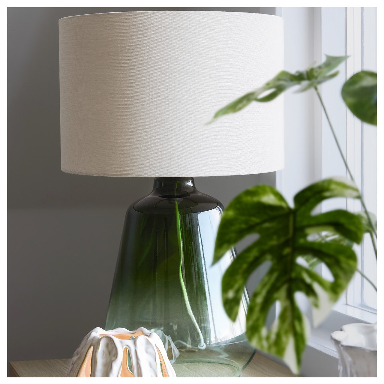Bordlampe med grønn glassfot og beige lampeskjerm.