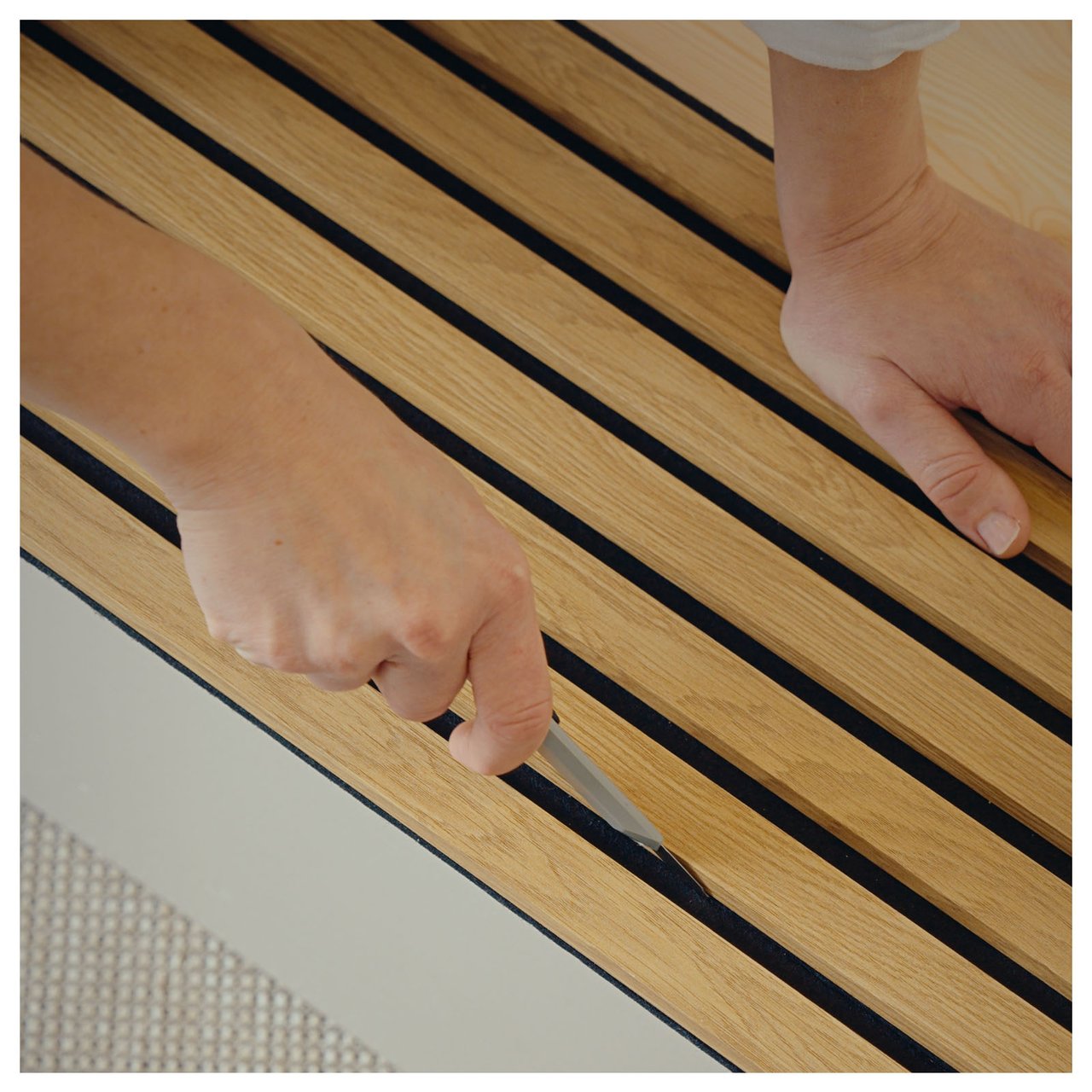 En person skär med kniv i mellanrummet på en akustikpanel.