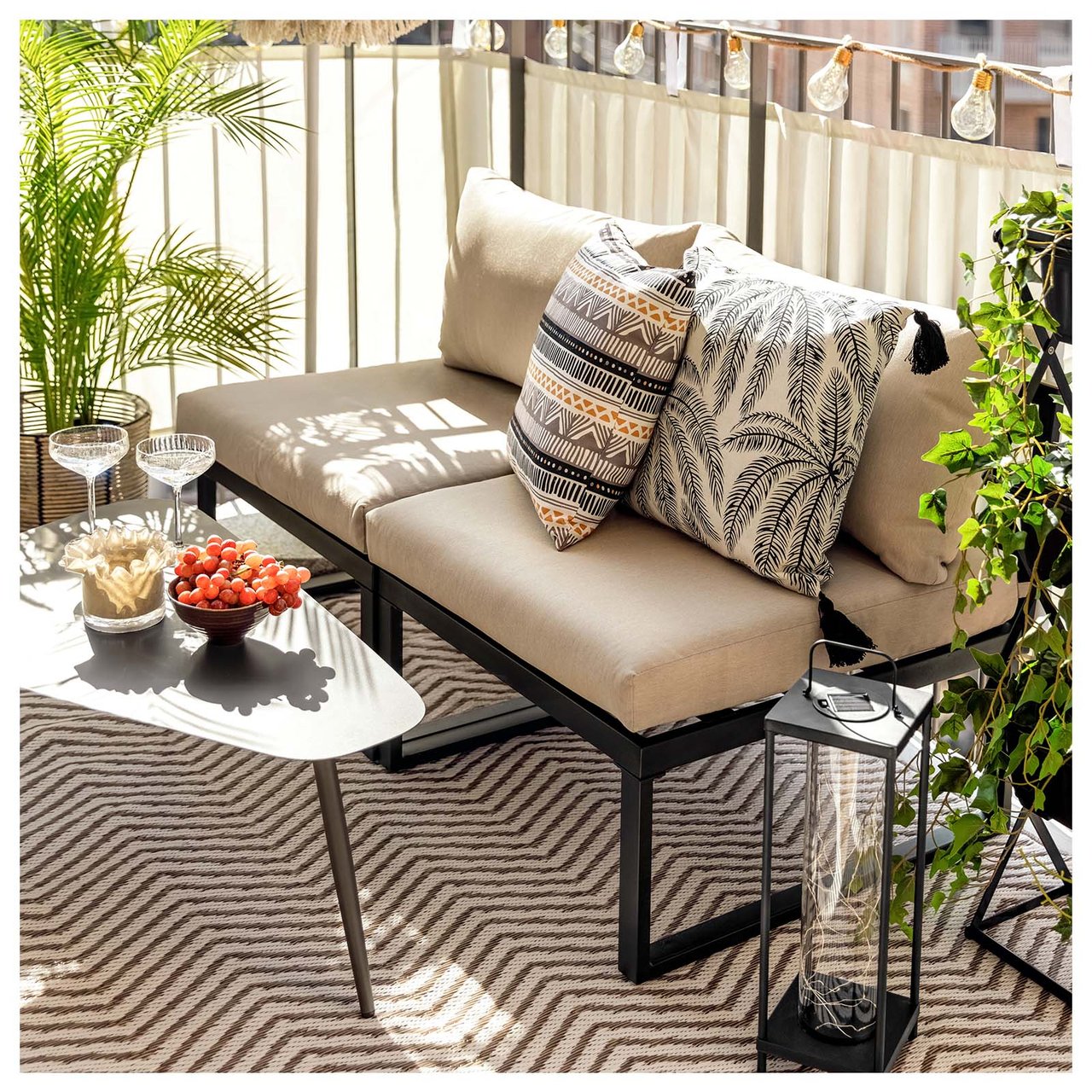 Del av balkong med innsynsskjerming, loungesofa, lite bord og puter i jordnære farger.