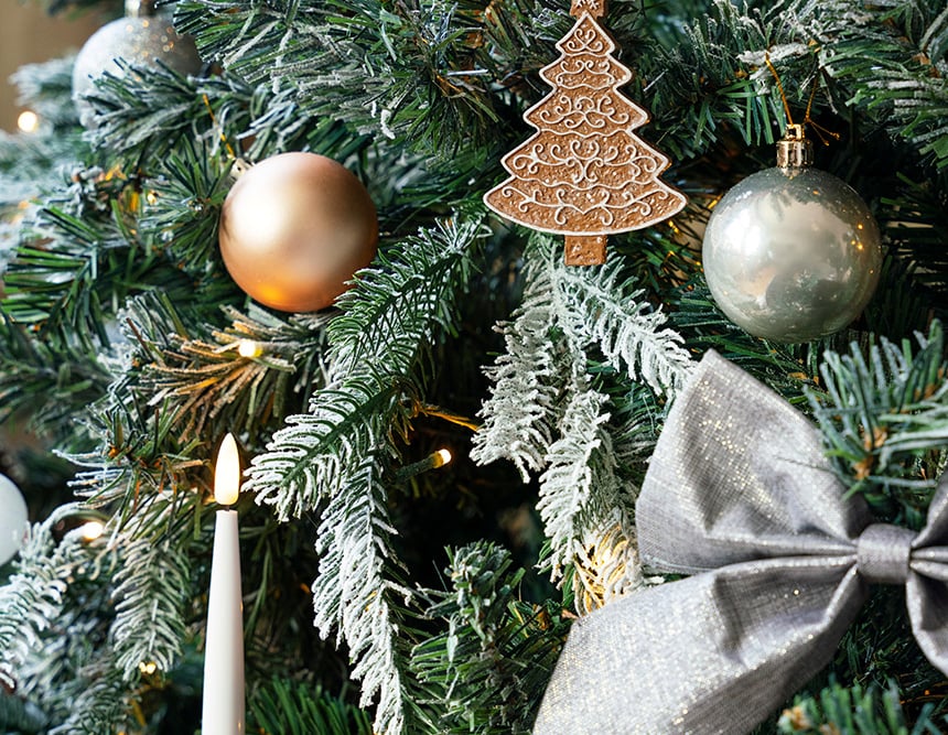 Lähikuva koristellusta joulukuusesta, jossa koristeita, valoja ja lumiefekti oksilla.