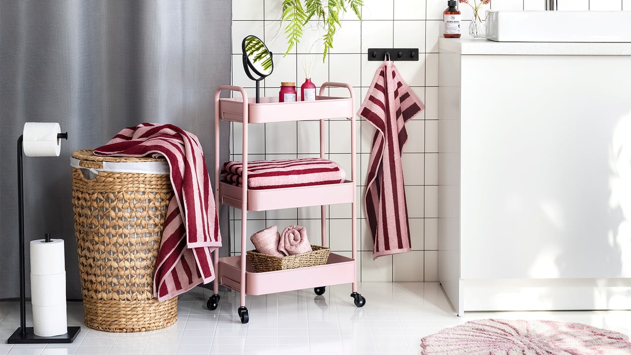 Badrum med rosa rullvagn och randiga handdukar i rött och rosa.