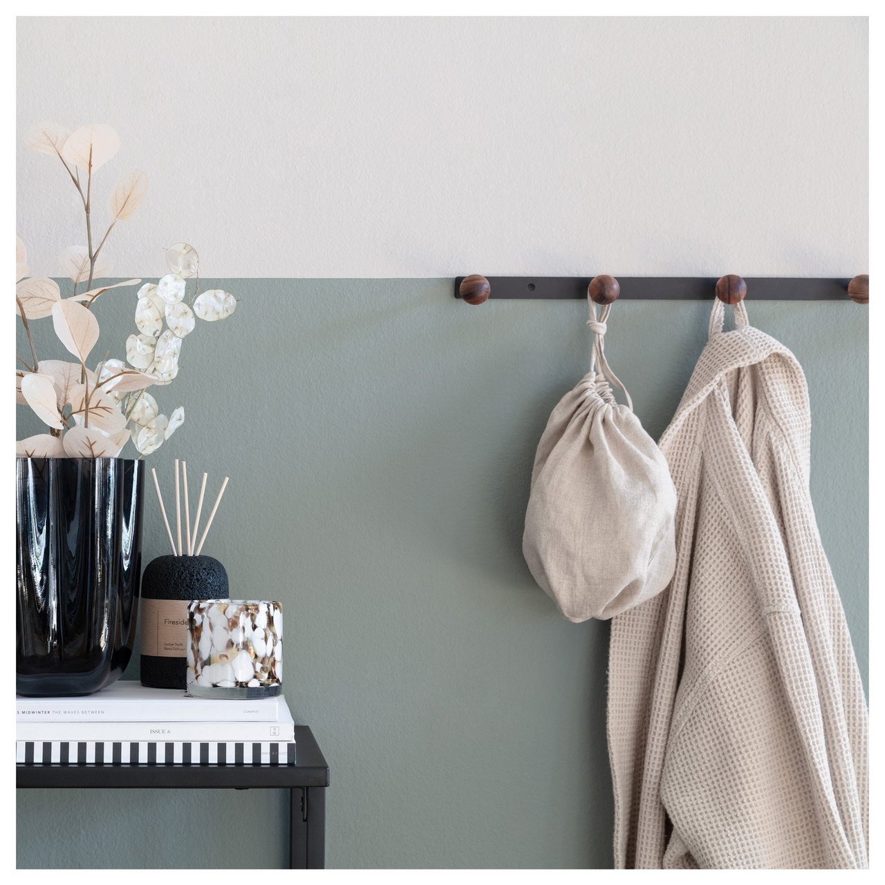 Flur mit Ablagetisch und Hakenleiste, an der Kleidung und eine Tasche vor einer Wand in Graugrün hängen.