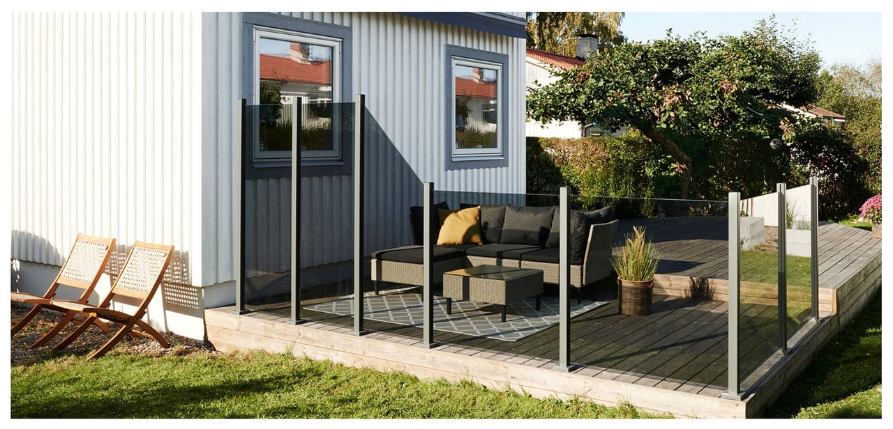 Stor träaltan som är inramad med gråtonade glasräcken framför en vit villa.