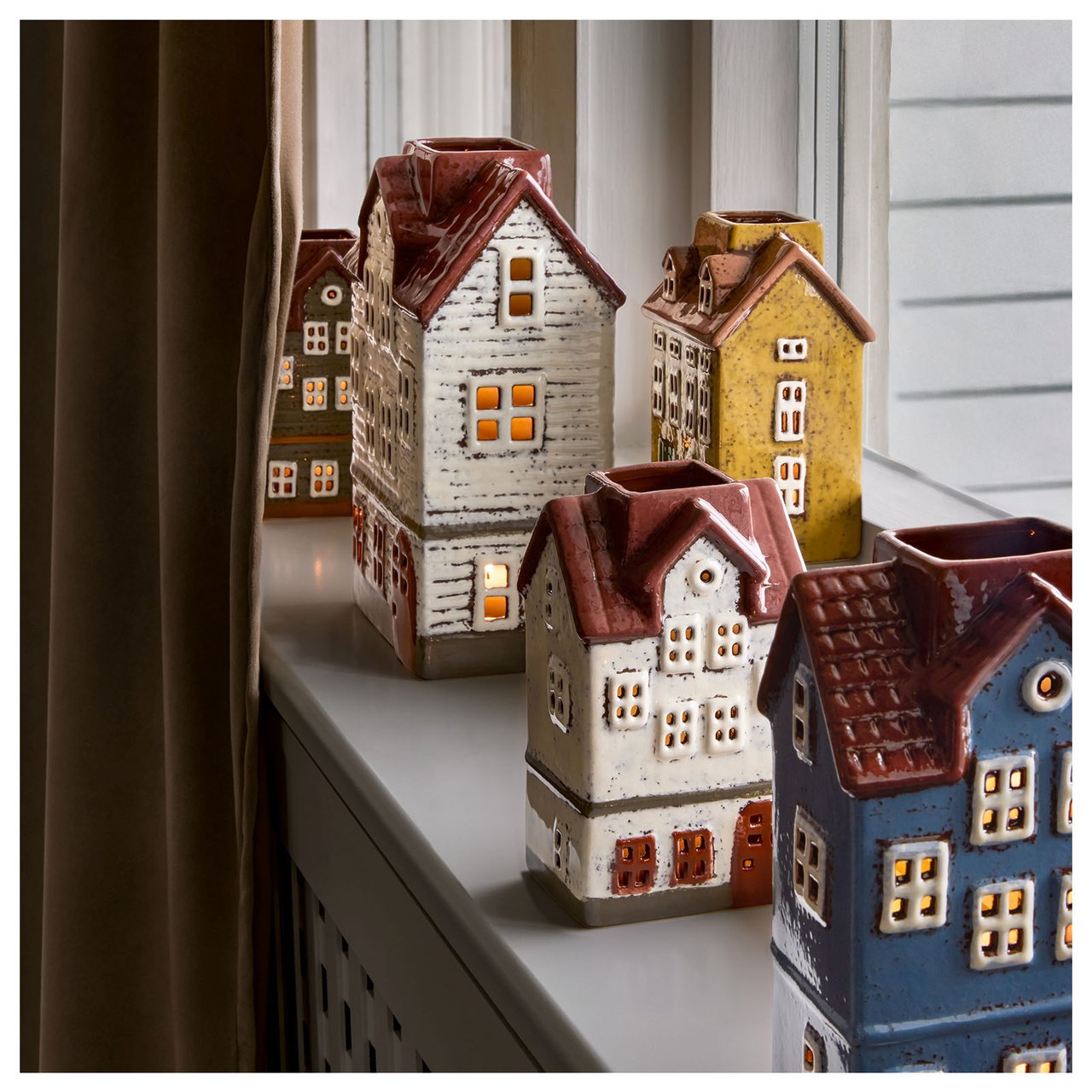 Fensterbank mit mehreren bunten Teelichthaltern in Form von Häusern.
