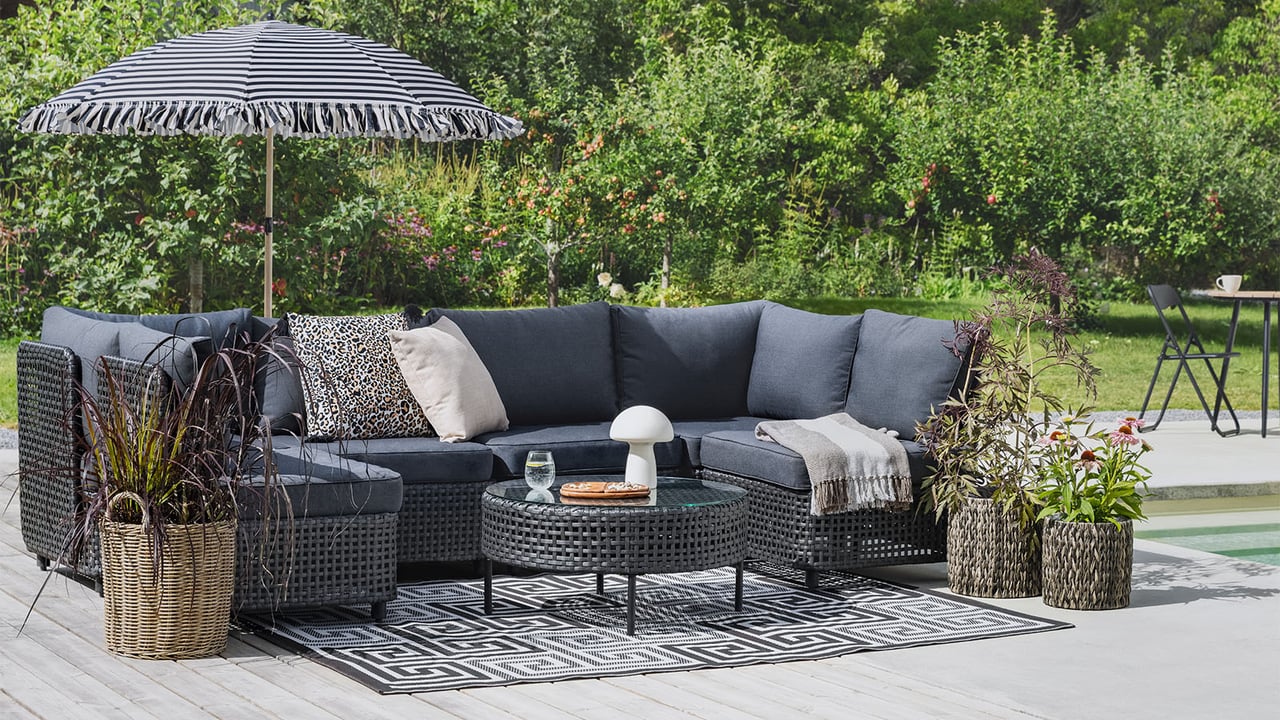 Utemiljö med svart loungegrupp i konstrotting och randigt parasoll.