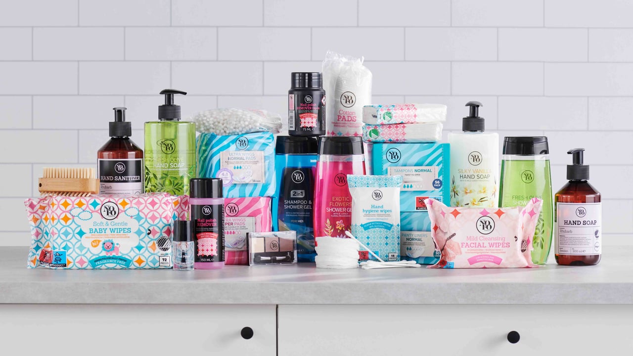 Hygienprodukter i olika förpackningar är uppställda på ett vitt bord mot kaklad vägg.