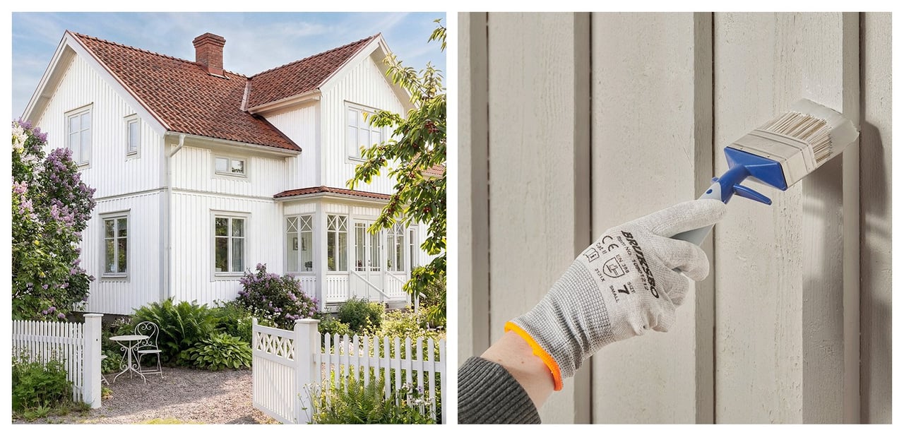 Stor vit villa innanför vitt trästaket. Hand som målar en grå träfasad med pensel.