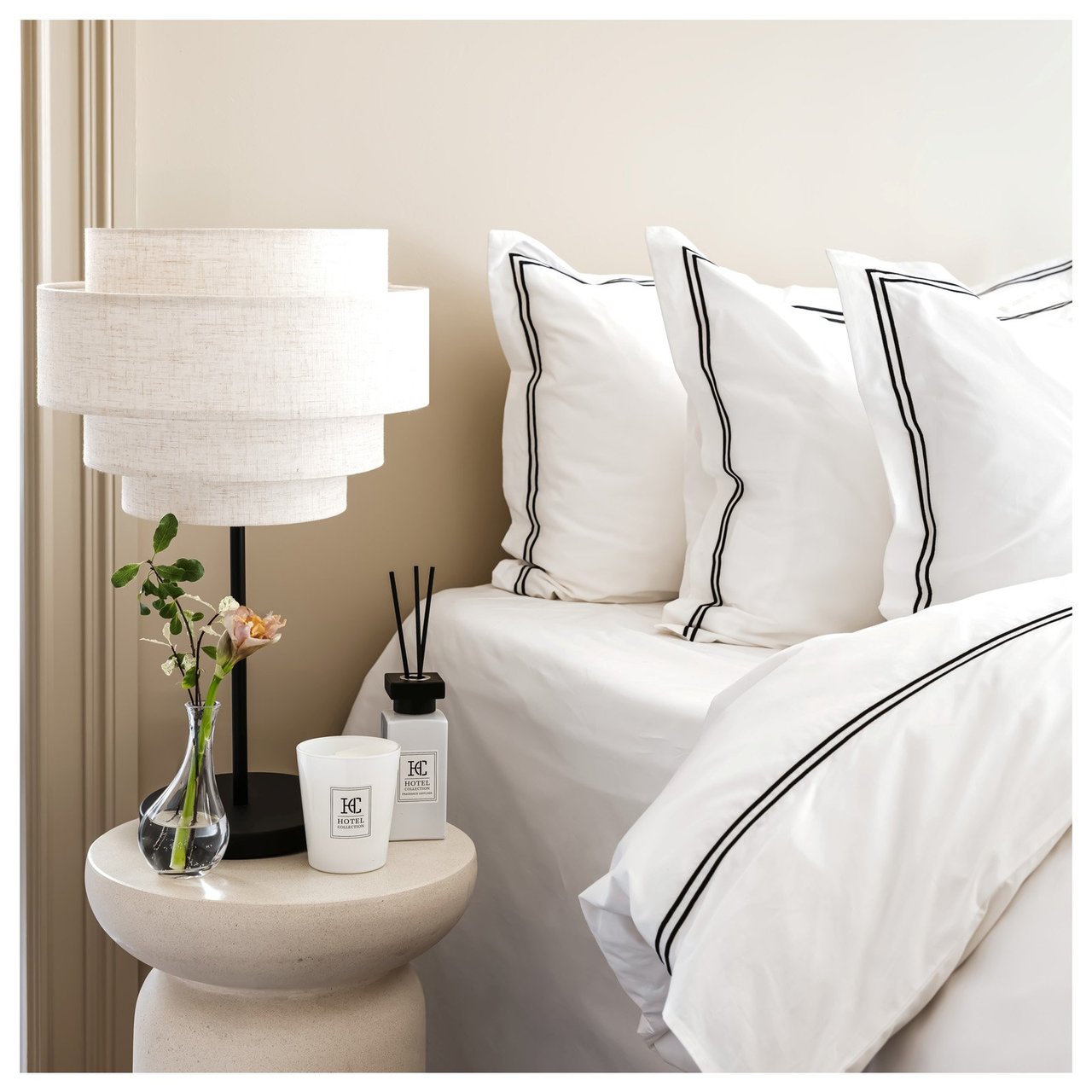 Säng med bäddtextilier i hotellstil och nattduksbord med lampa och dekorationer.