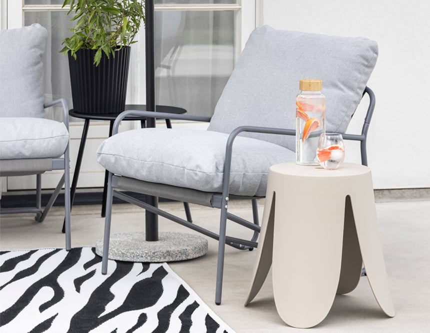 Moderne Terrasse mit grauen Sesseln, zebragemustertem Teppich, beigem Beistelltisch und Glas mit Zitrusgetränk.