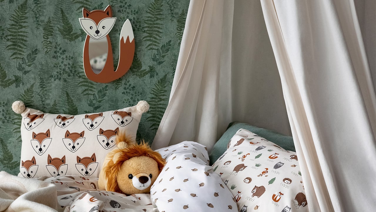 Säng bäddad med djurmönstrade textilier. Vägglampa i form av en räv hänger på väggen.
