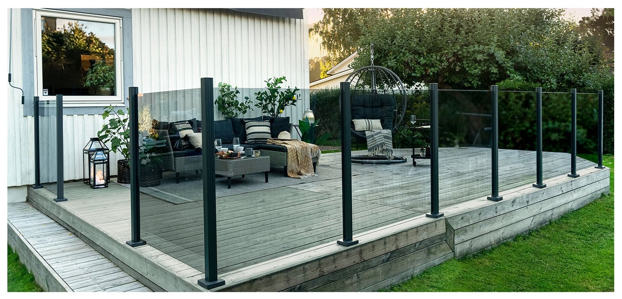 Stor träaltan framför vit villa som är inramad med gråtonade glasräcken.