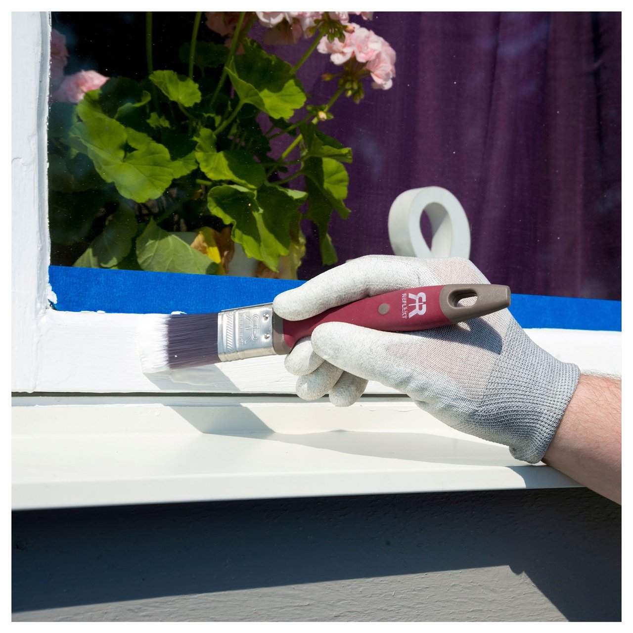 En hand med målarhandske målar fönsterkarm i vitt med smal pensel.