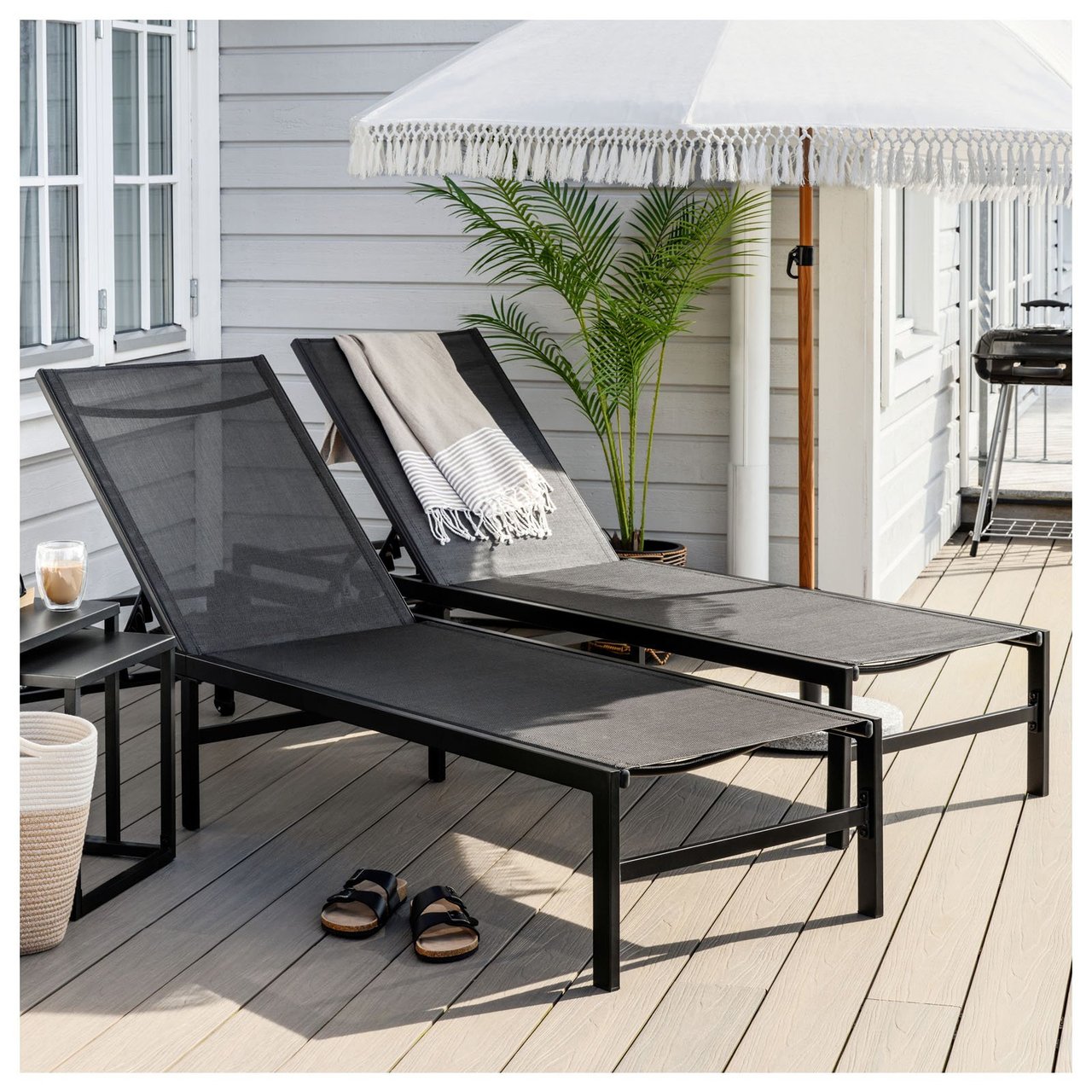 Zwei Sonnenliegen auf einer sonnigen Terrasse mit Sonnenschirm.