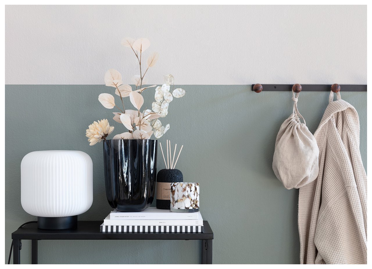 Musta sivupöytä eteisessä kaksiväristä seinää vastapäätä, jolla on koukut ja ripustettuja vaatteita.