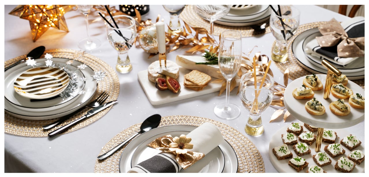 Elegante Neujahrstafel in Weiß und Gold mit Geschirr, Servietten und festlicher Deko.