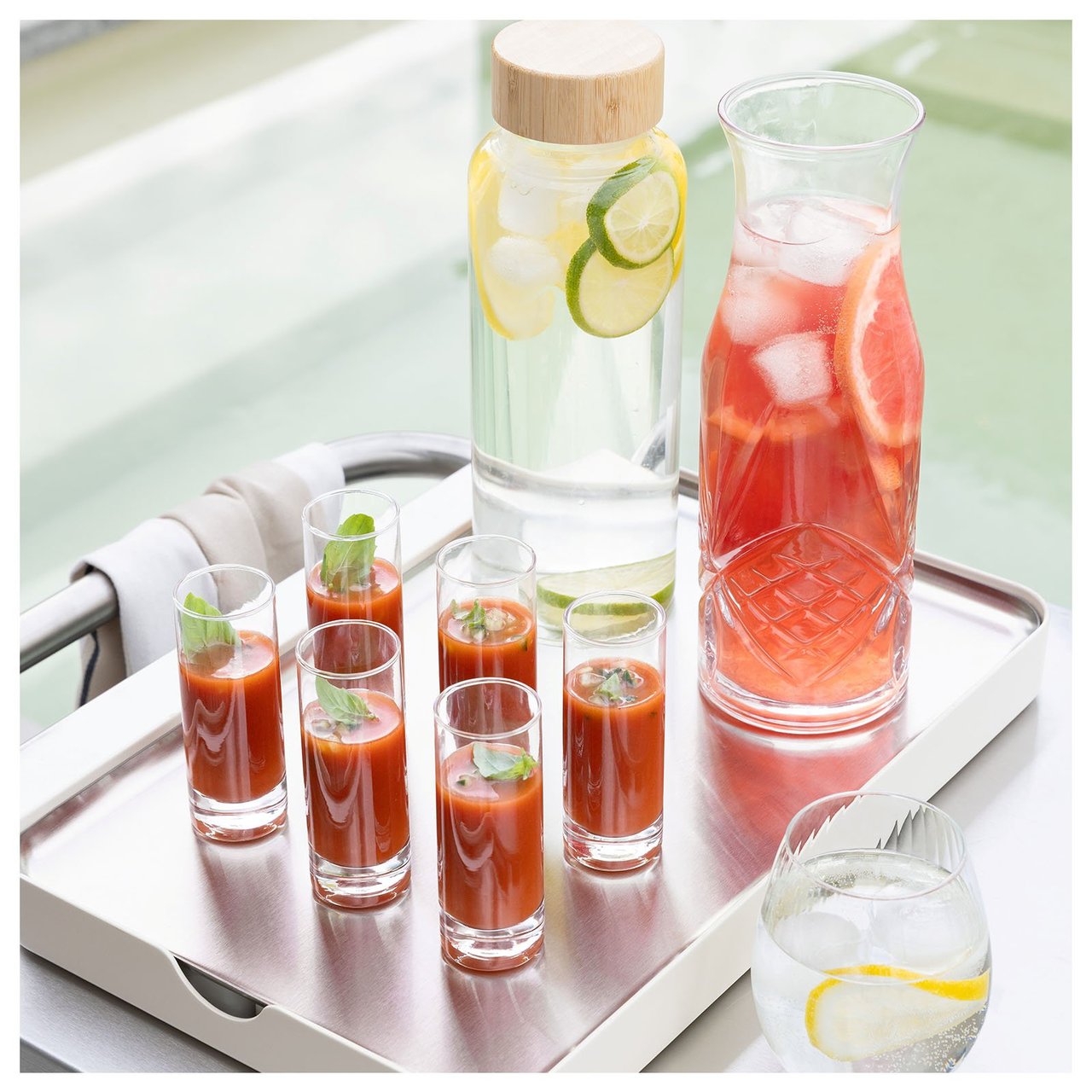 Sex små glas och två karaffer står på en kylbricka vid en pool.