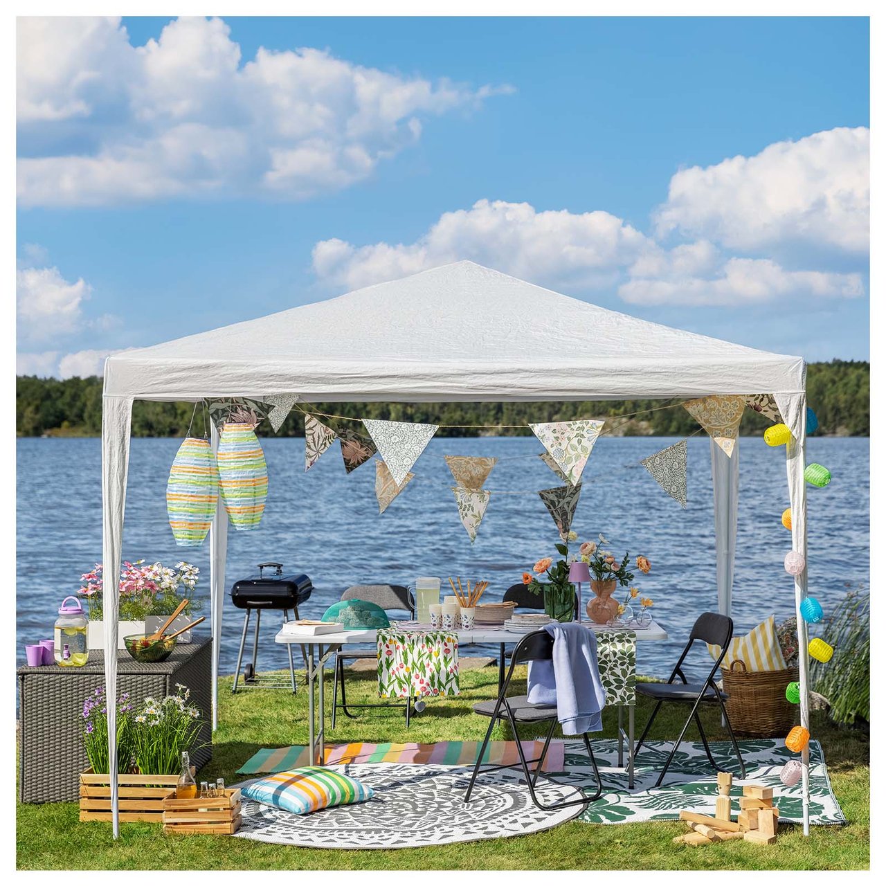 Gemütliche Terrasse am Wasser mit Teppichen auf dem Boden. Stühle und Tisch sind von einem Pavillon mit hängenden Reispapierleuchten eingerahmt.