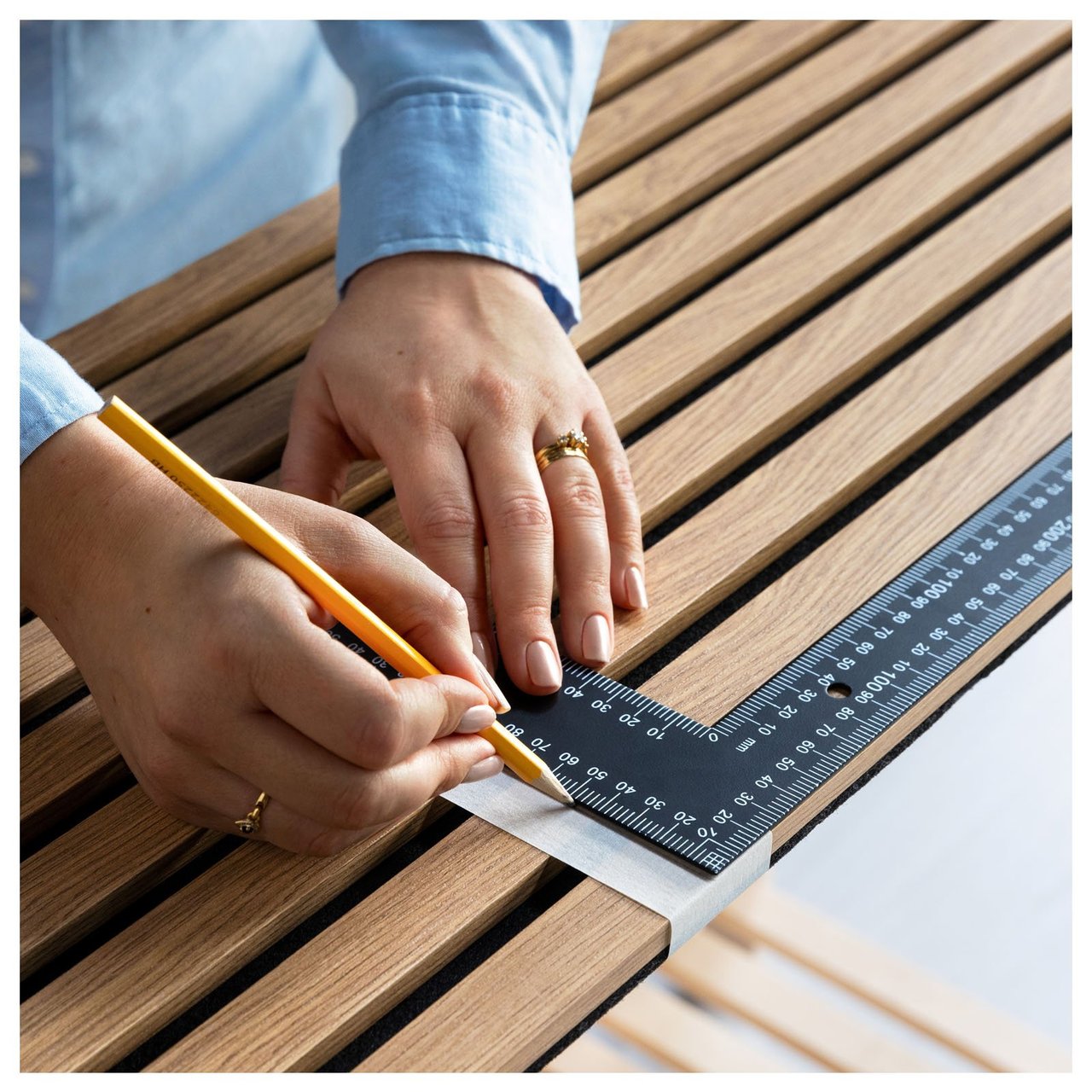 En person markerar mått på en akustikpanel med blyertspenna och vinkelhake.