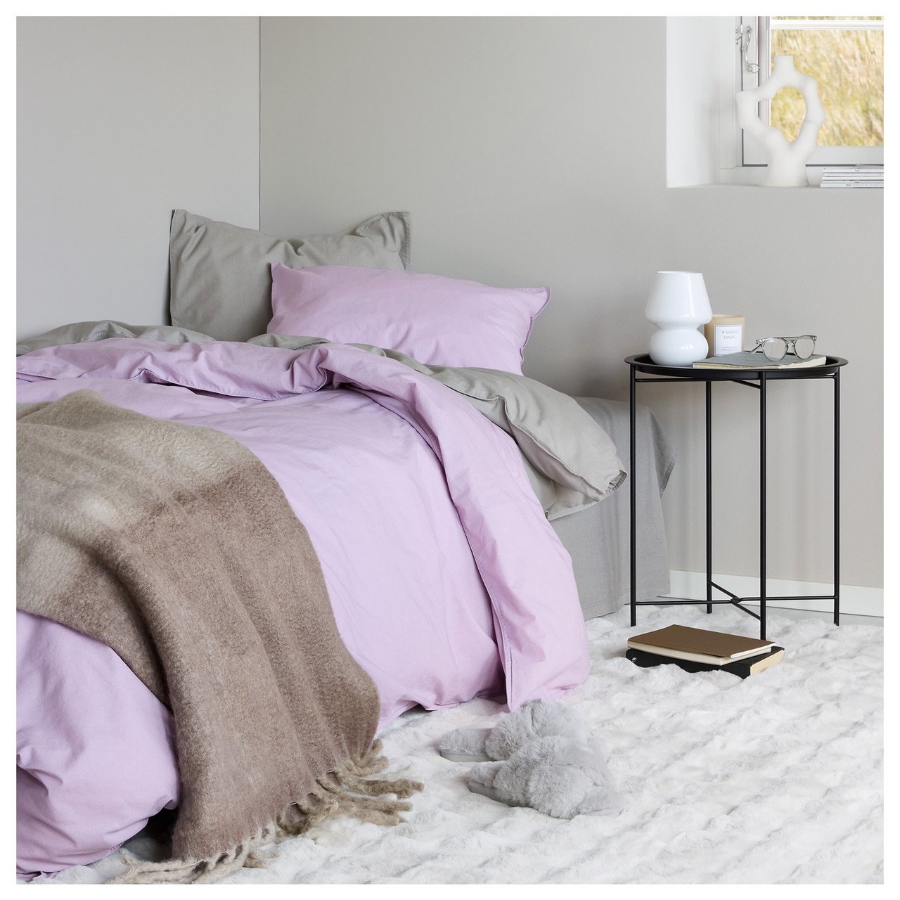 Schlafzimmer mit einem gemachten Bett, Ablagetisch und dekorativen Details in einer hellen und gemütlichen Atmosphäre.