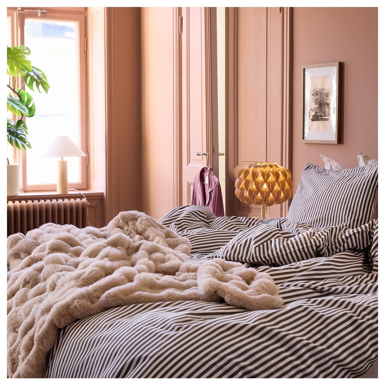 Ett sovrum med terrakottafärgade väggar, randiga sängkläder och en fluffig, beige pläd.