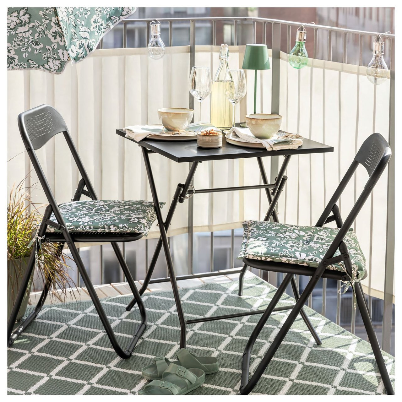 Ein sonniger Balkon mit Balkonmöbeln auf einem gemusterten Outdoor-Teppich. Polsterauflagen und Sonnenschirm haben das gleiche Muster.