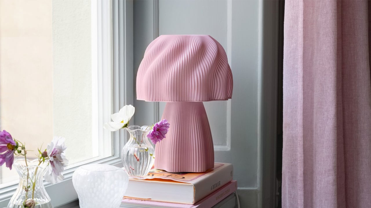 Skulpturell bordlampe står i vinduskarmen med bøker og vaser.