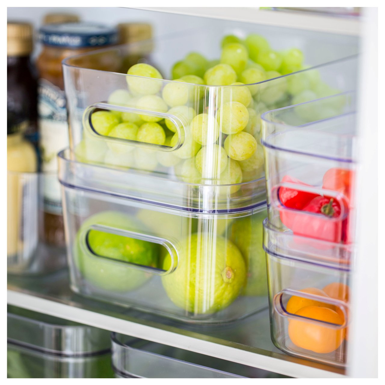 Kjøleskap organisert med gjennomsiktige oppbevaringsbokser fylt med frukt og grønnsaker.