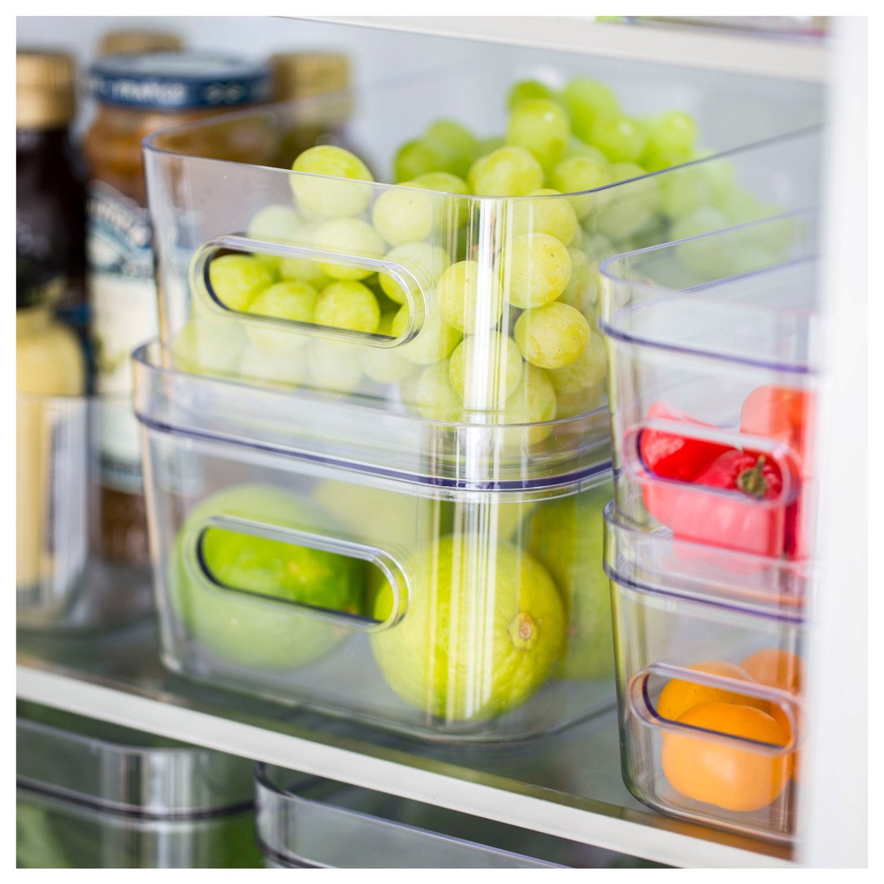Kjøleskap organisert med gjennomsiktige oppbevaringsbokser fylt med frukt og grønnsaker.