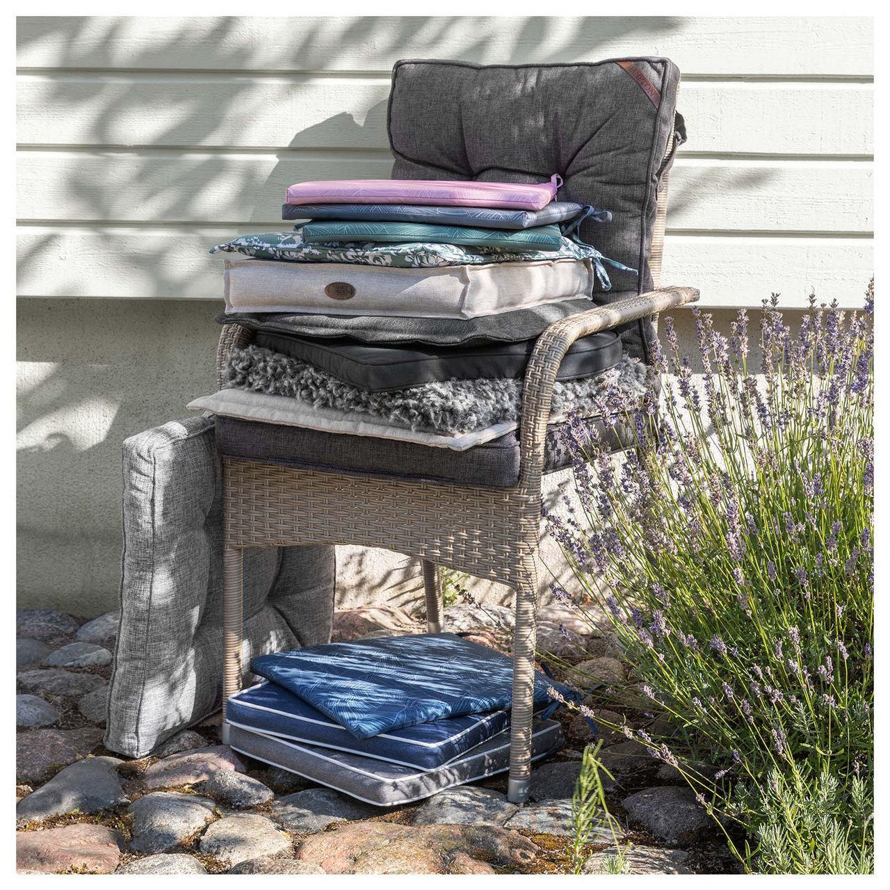 Gartenstuhl aus Kunstrattan vor einer Hausfassade mit verschiedenen Kissen auf der Sitzfläche und unter dem Stuhl.