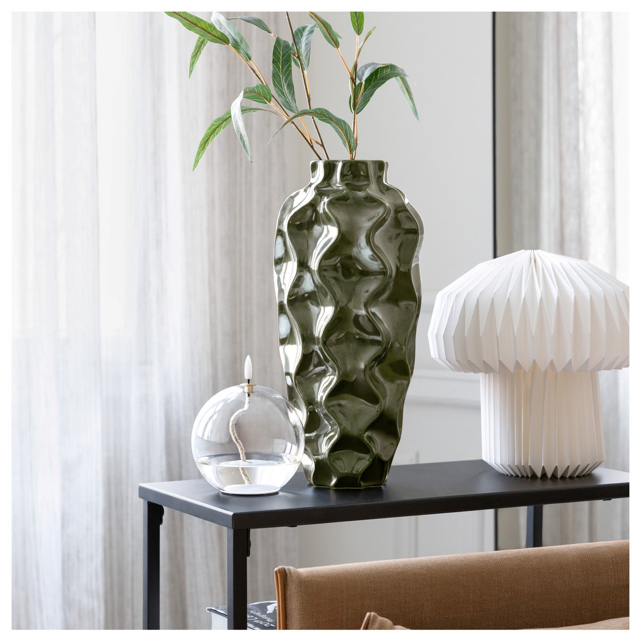 Dekorative Vase, Lampe und Öllampe auf einem schwarzen Beistelltisch in einem hellen Raum.