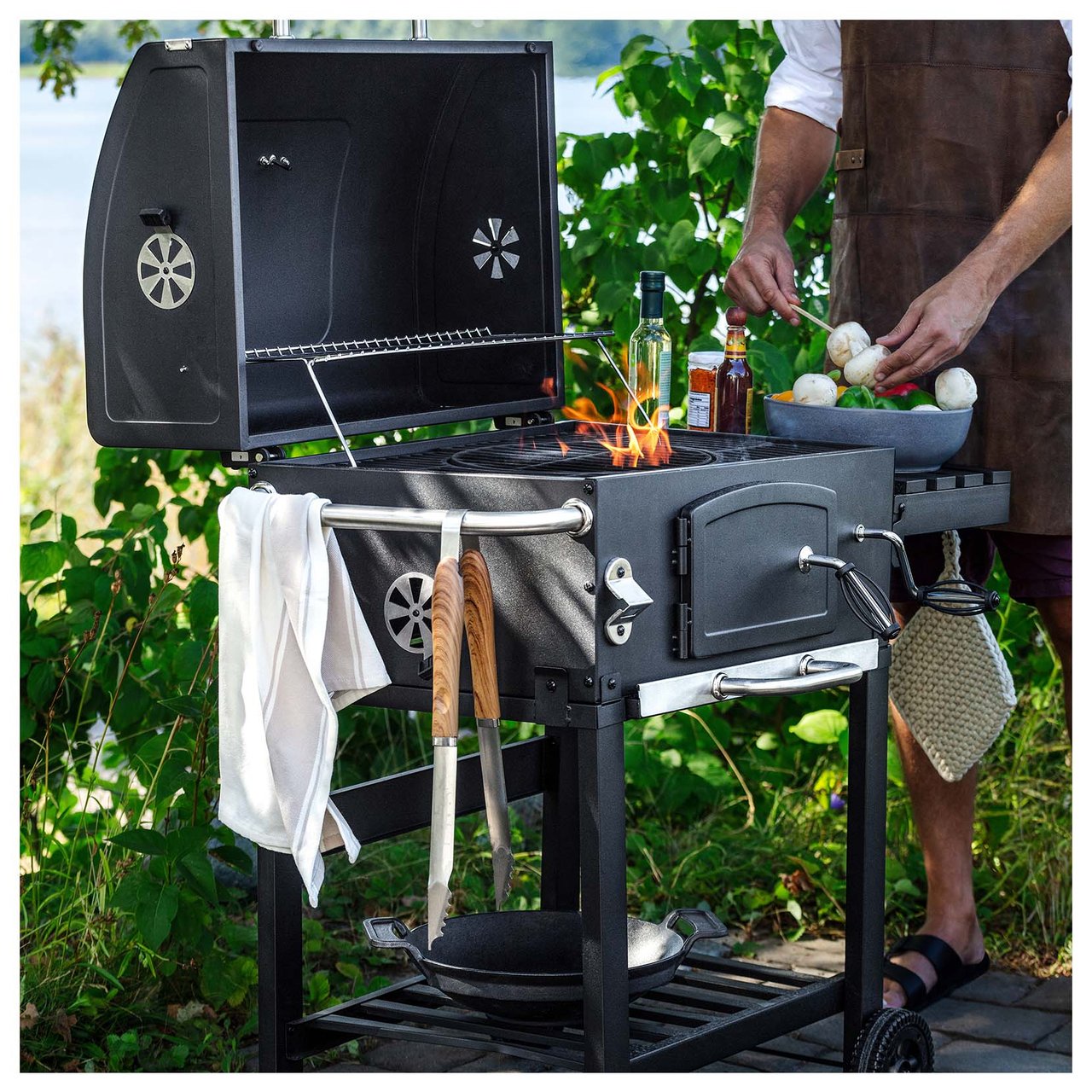 Eine Person mit Schürze bereitet im Freien Gemüsespieße auf dem Grill zu.