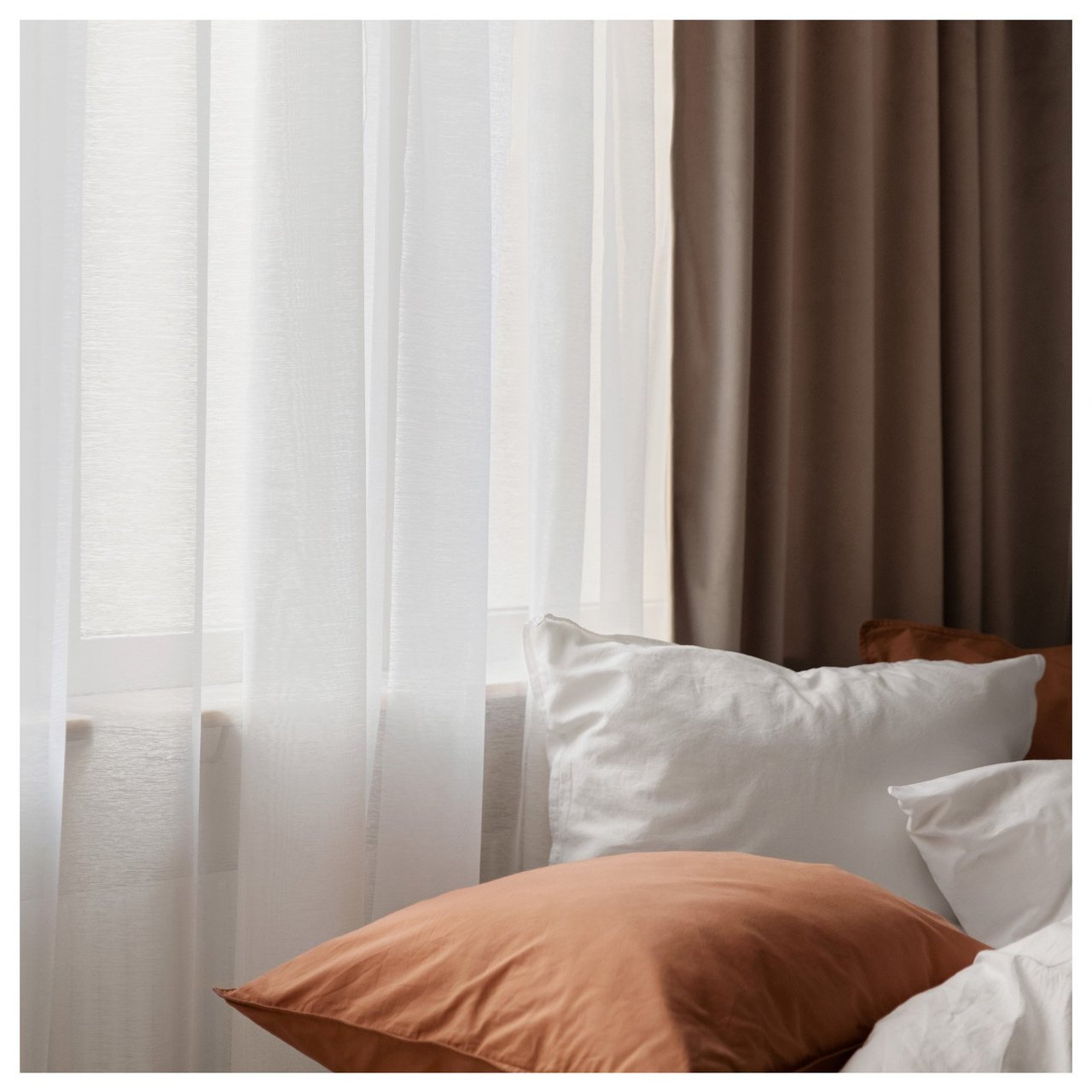 Bett an einem Fenster mit durchsichtigen, hellen Vorhängen und dickeren dunklen Vorhängen.