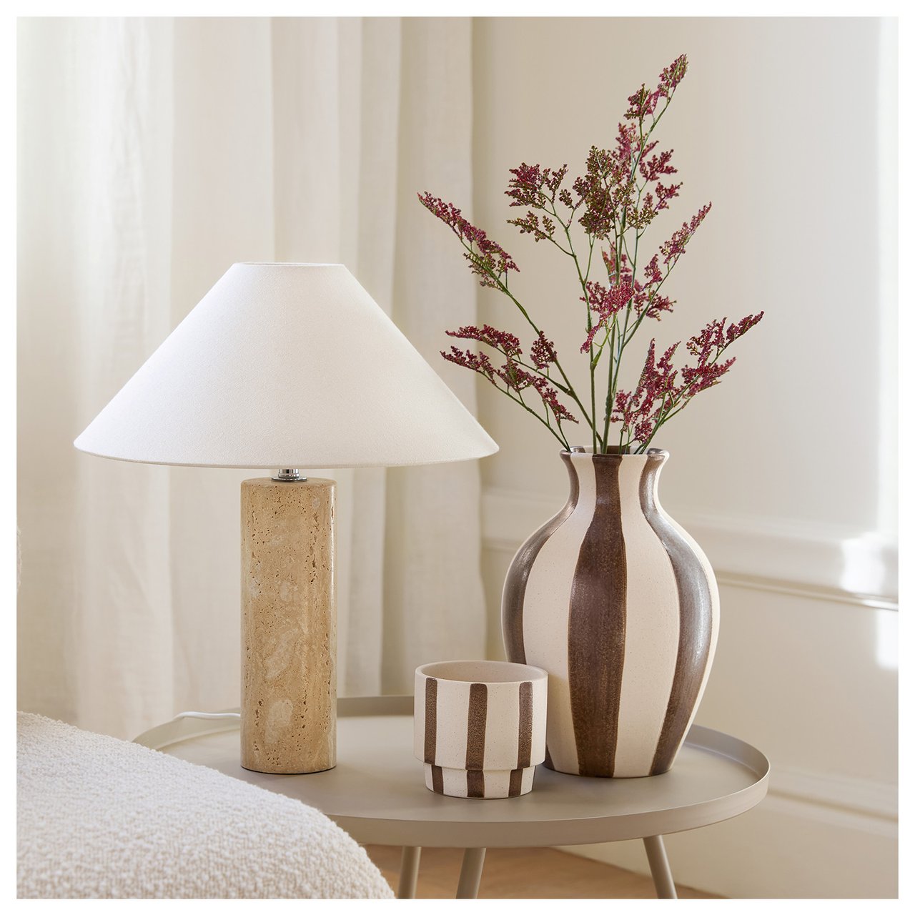 Lite sidebord med lampe og høy brun- og hvitstripet vase. I vasen står vinrød risp.