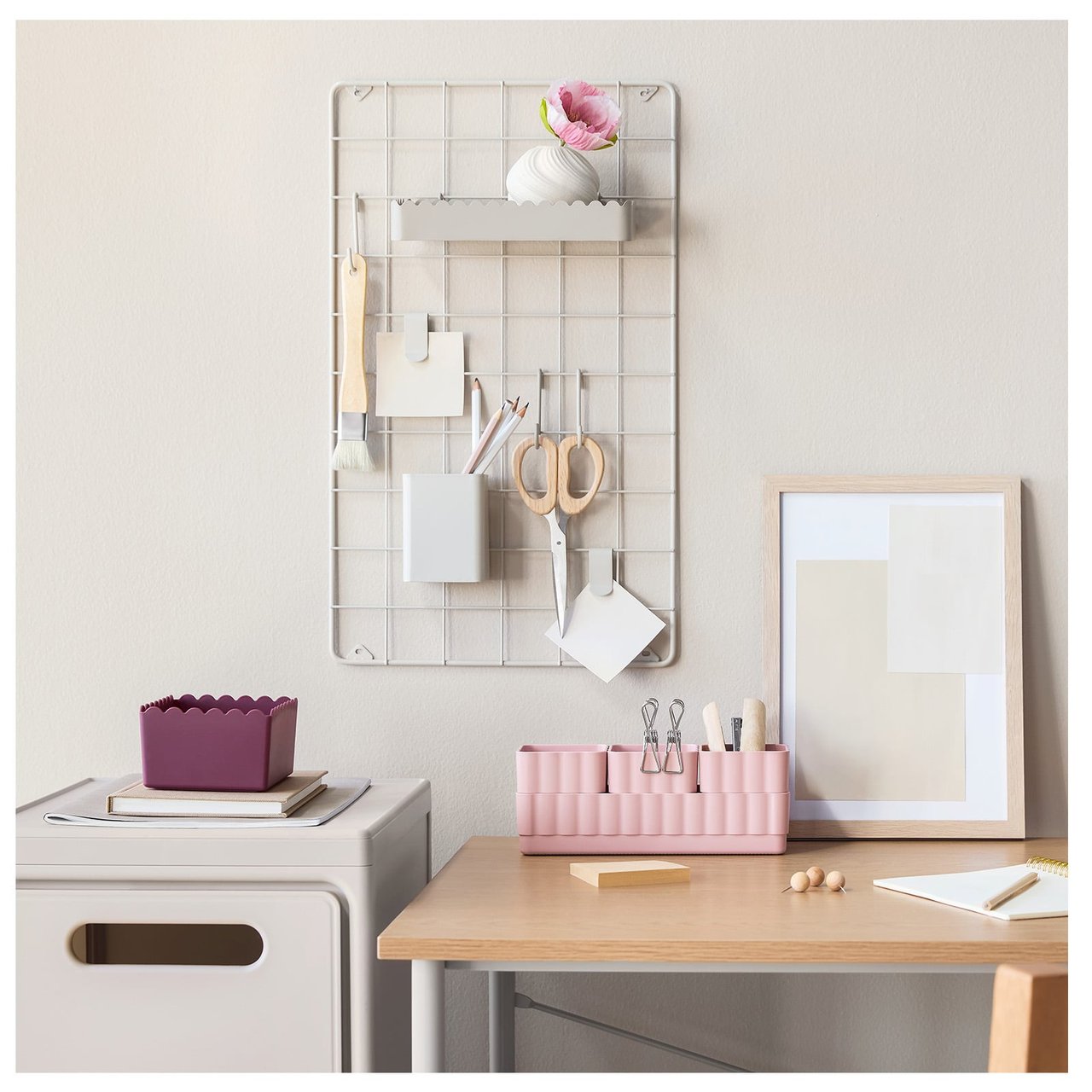 Skrivbord med rosa organizers, anslagstavla i beige metall och en lådhurts i beige.