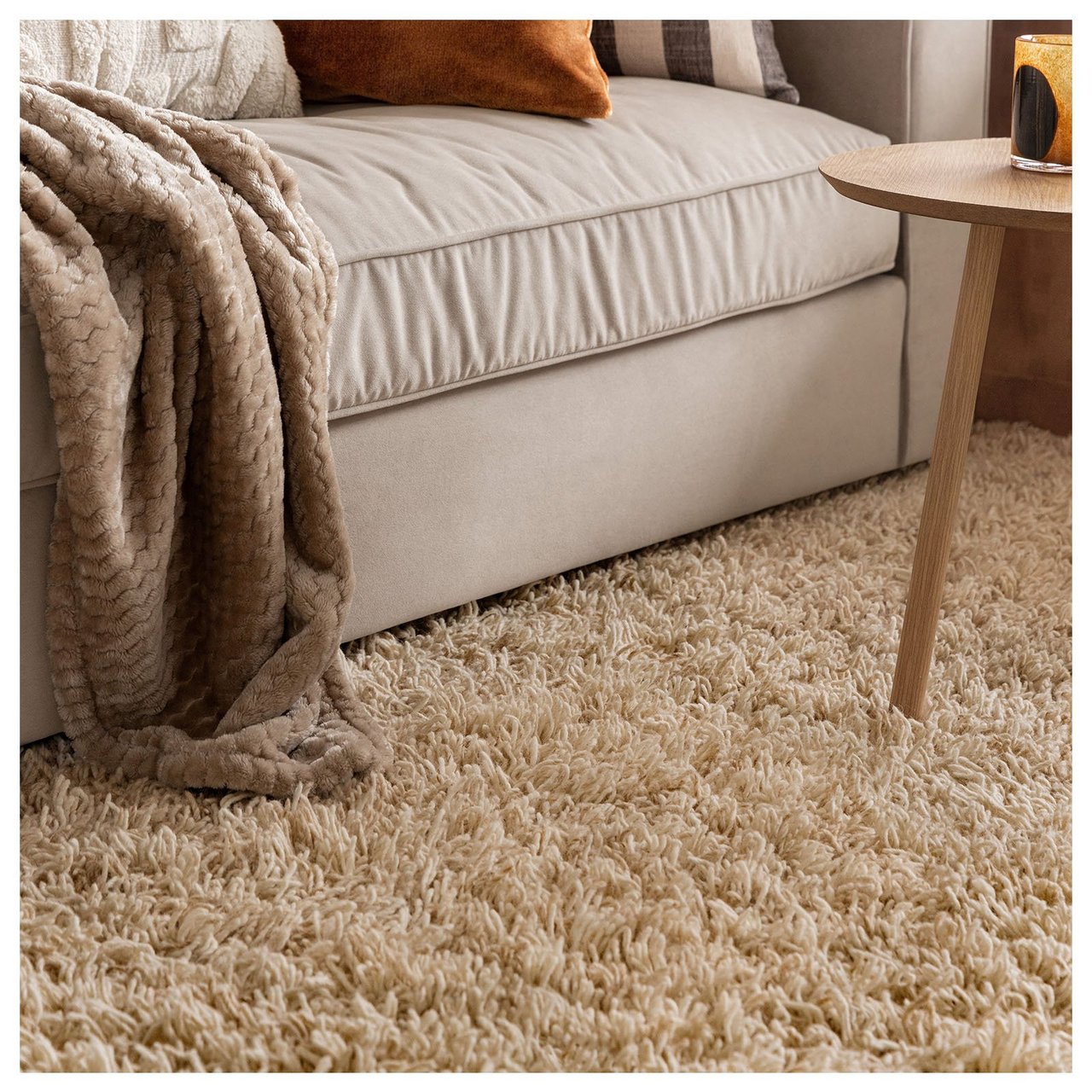 Beigefarbener, langfloriger Teppich unter beigem Sofa.