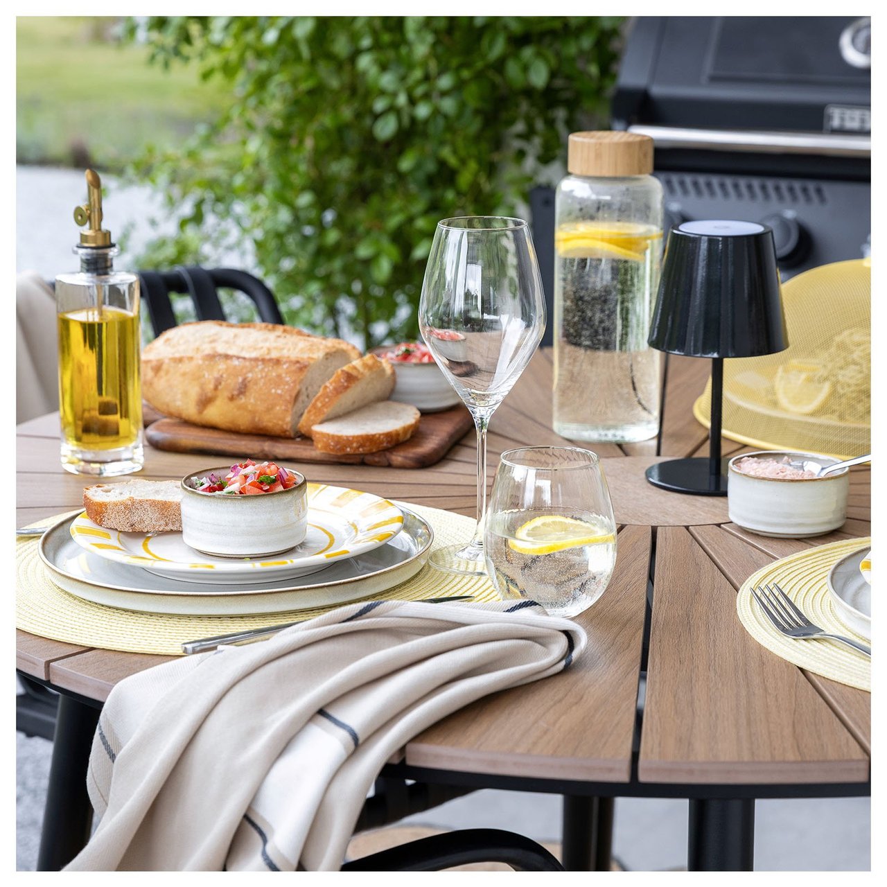 Ett dukat bord utomhus med gula bordstabletter och gulrandigt porslin. 