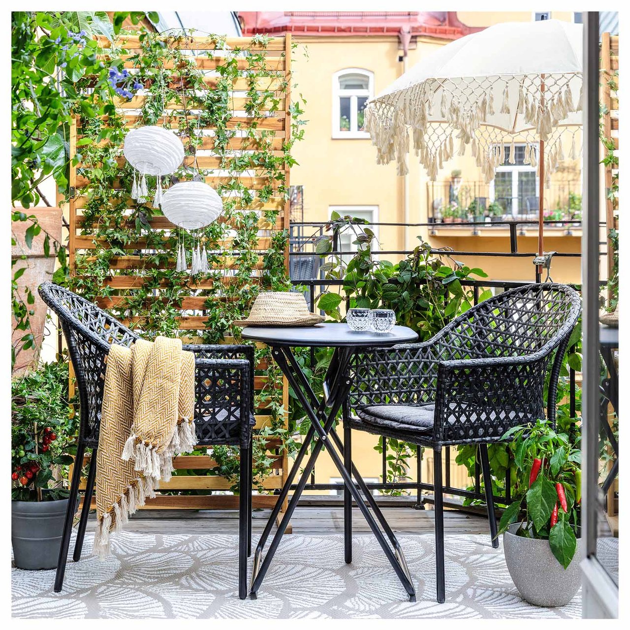 Balkong mot bakgård med to stoler i kunstrotting og et lite sammenleggbart bord.