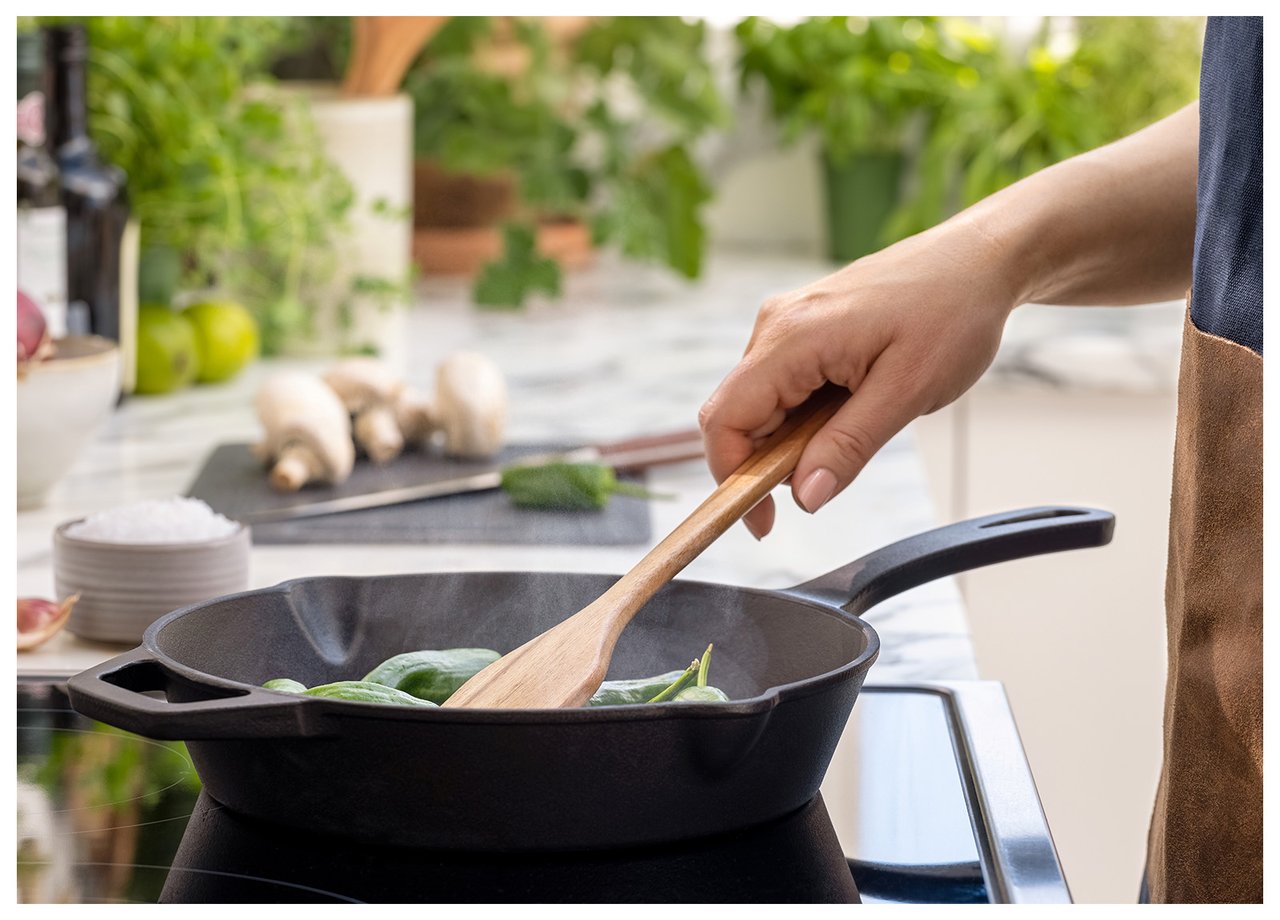 Hånd som rører med tresleiv i en stekepanne av støpejern.
