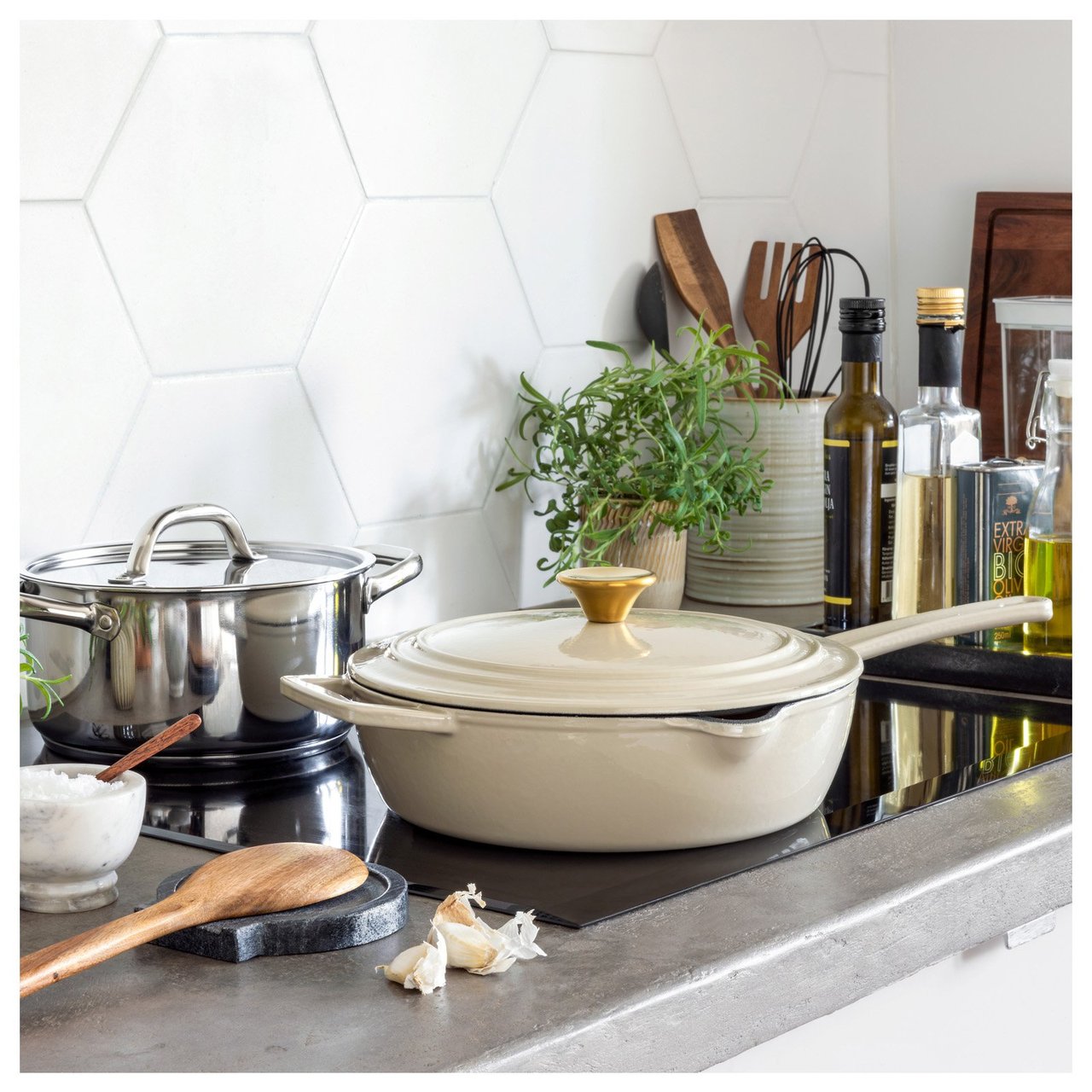 Spishäll med kastruller, redskap, färska örter och oljor i ett stilrent kök.