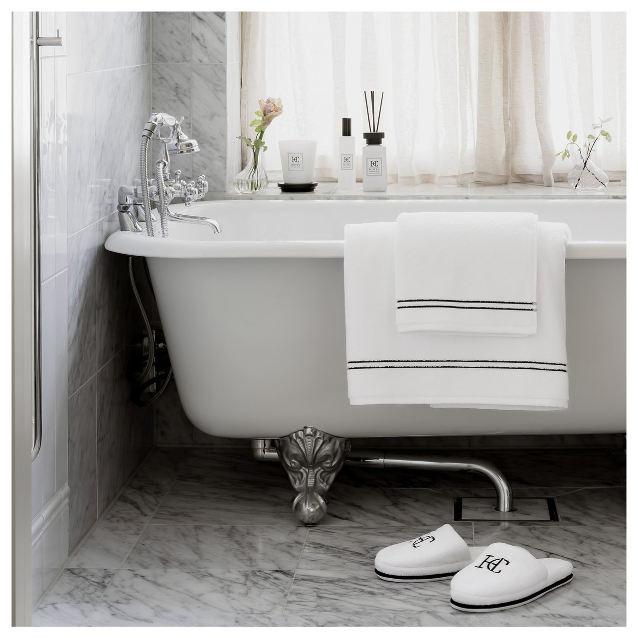 Badewanne mit weißen Handtüchern, die über den Rand der Badewanne gelegt sind, und weißen Pantoffeln auf dem Boden.