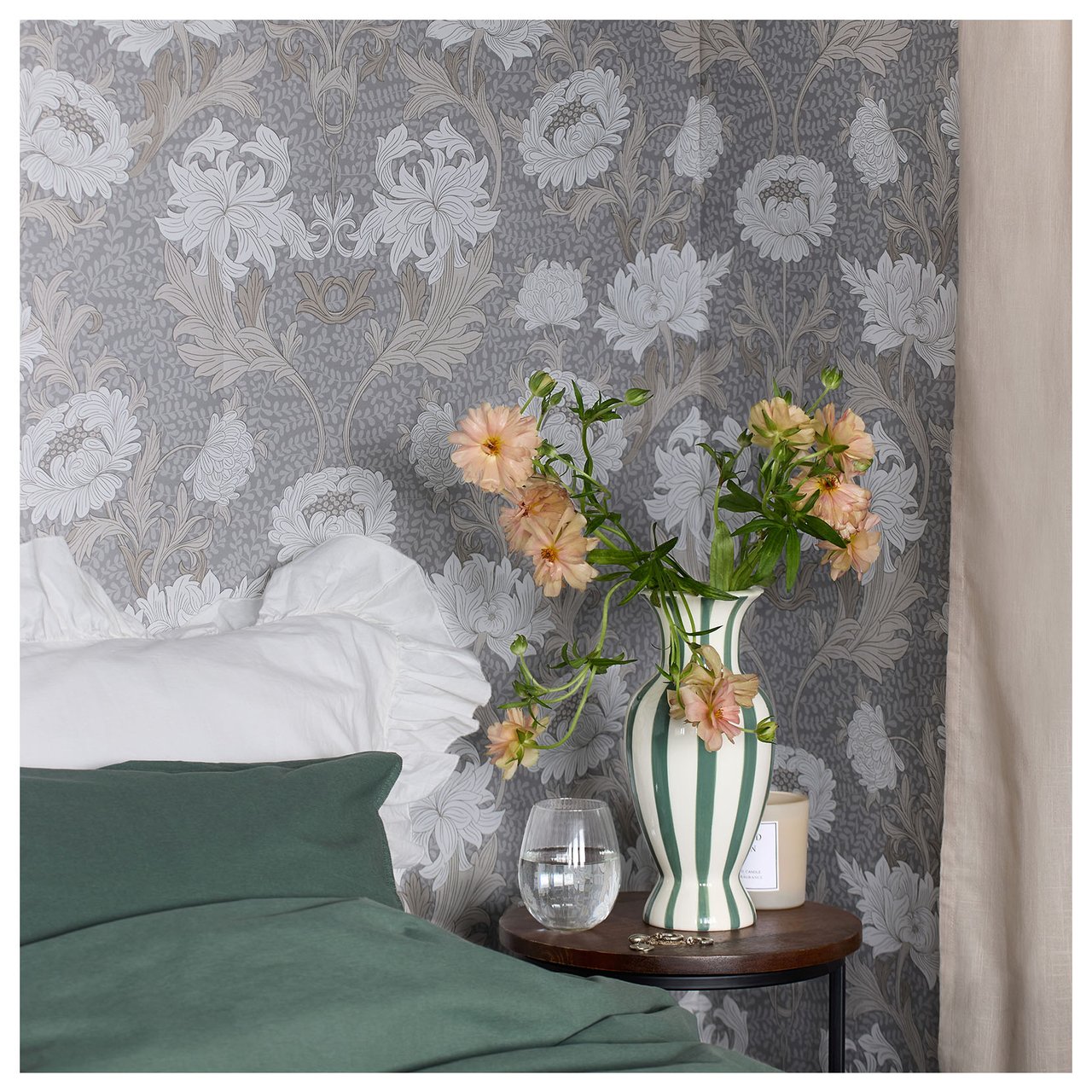 Makuuhuone, jossa on sijattu sänky ja yöpöytä, jolla on maljakko ja kukkia ja seinällä kuviollinen tapetti.