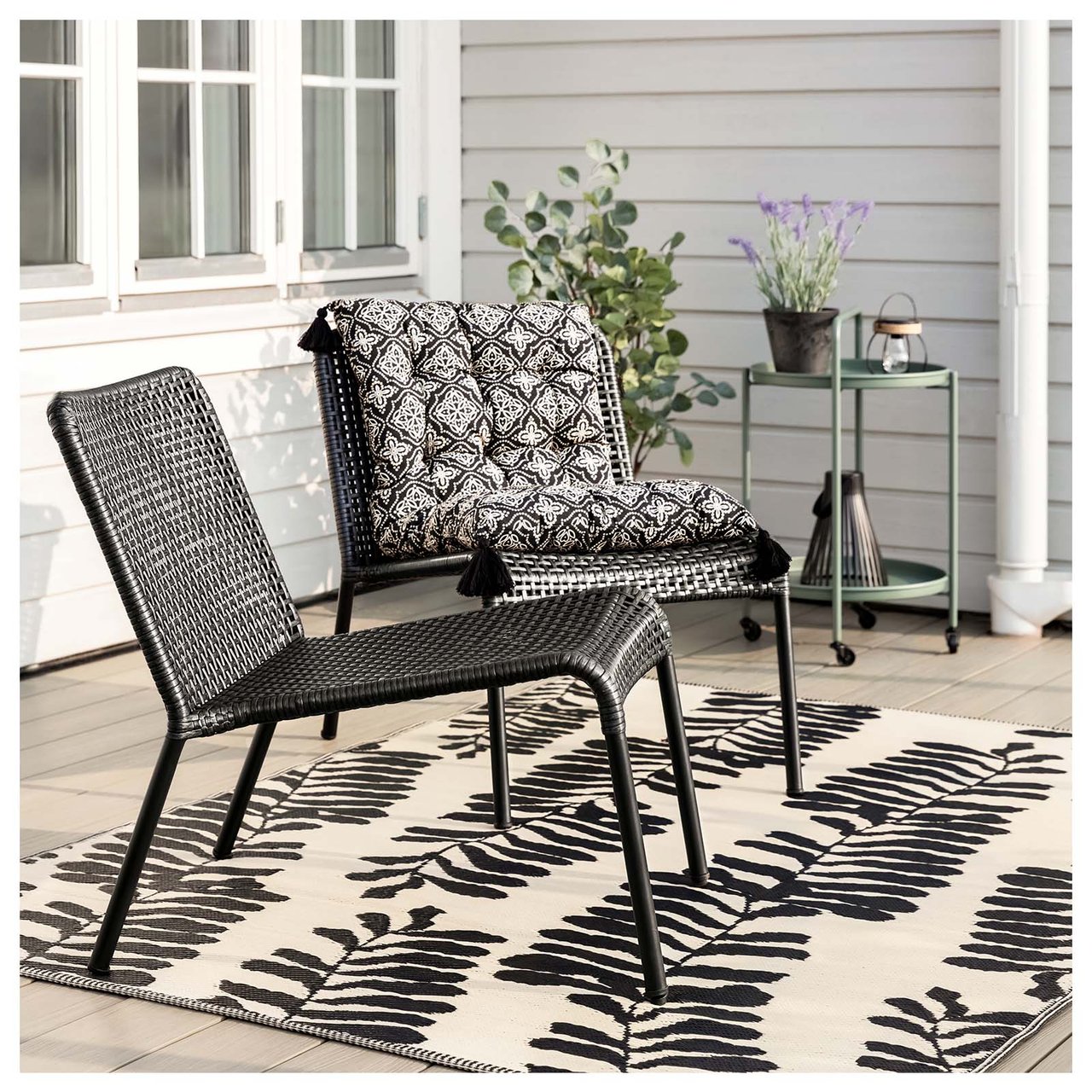 Zwei Stühle im Freien auf einem weichen, gemusterten Teppich in Schwarz und Beige auf der Terrasse eines Hauses.