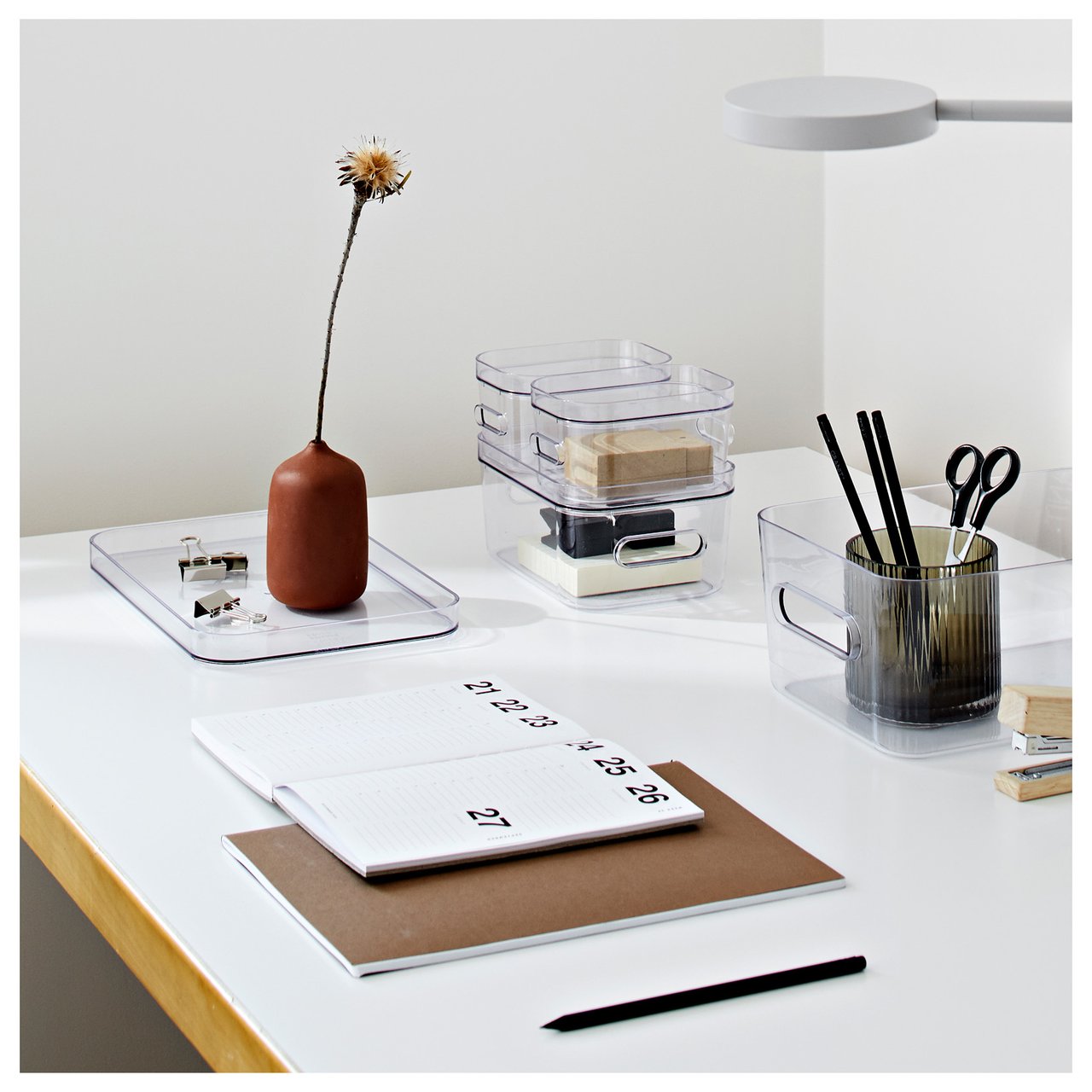 Ordentlich organisierte Arbeitsfläche mit Notizblöcken und transparenten Aufbewahrungsboxen mit Schreibtischutensilien.
