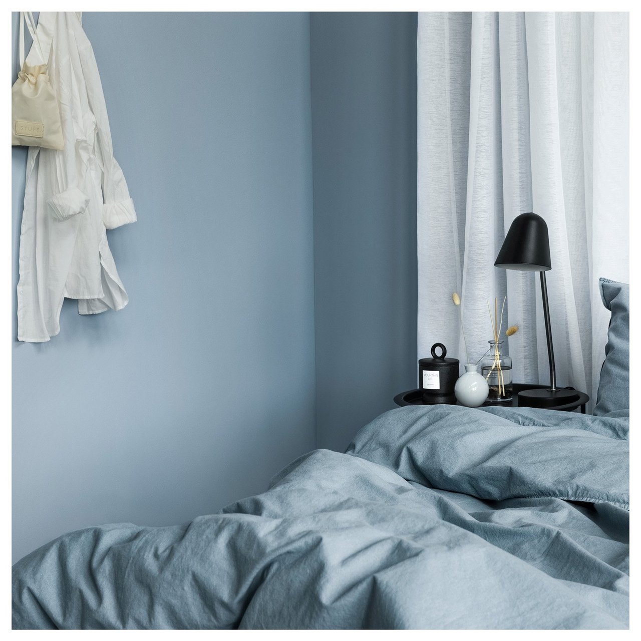Makuuhuone, jossa on sängyt, yöpöydät ja sinisävyiset seinät. Valkoinen paita riippuu seinällä.