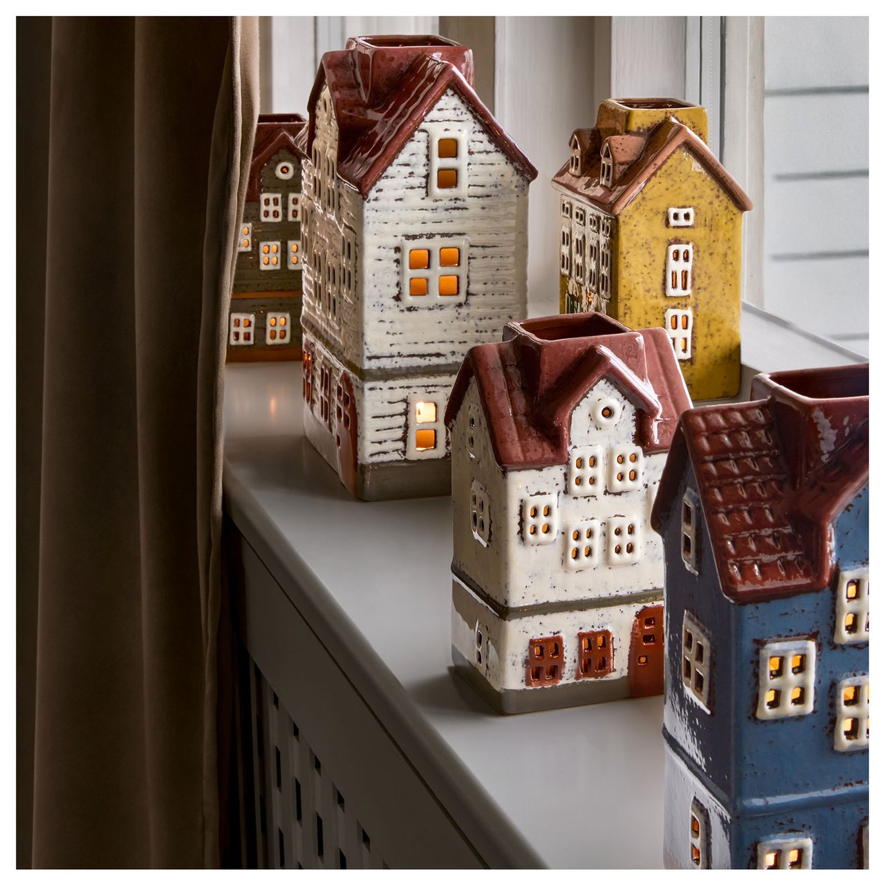 Mehrere Teelichthalter in Form von Häusern stehen auf einer Fensterbank.