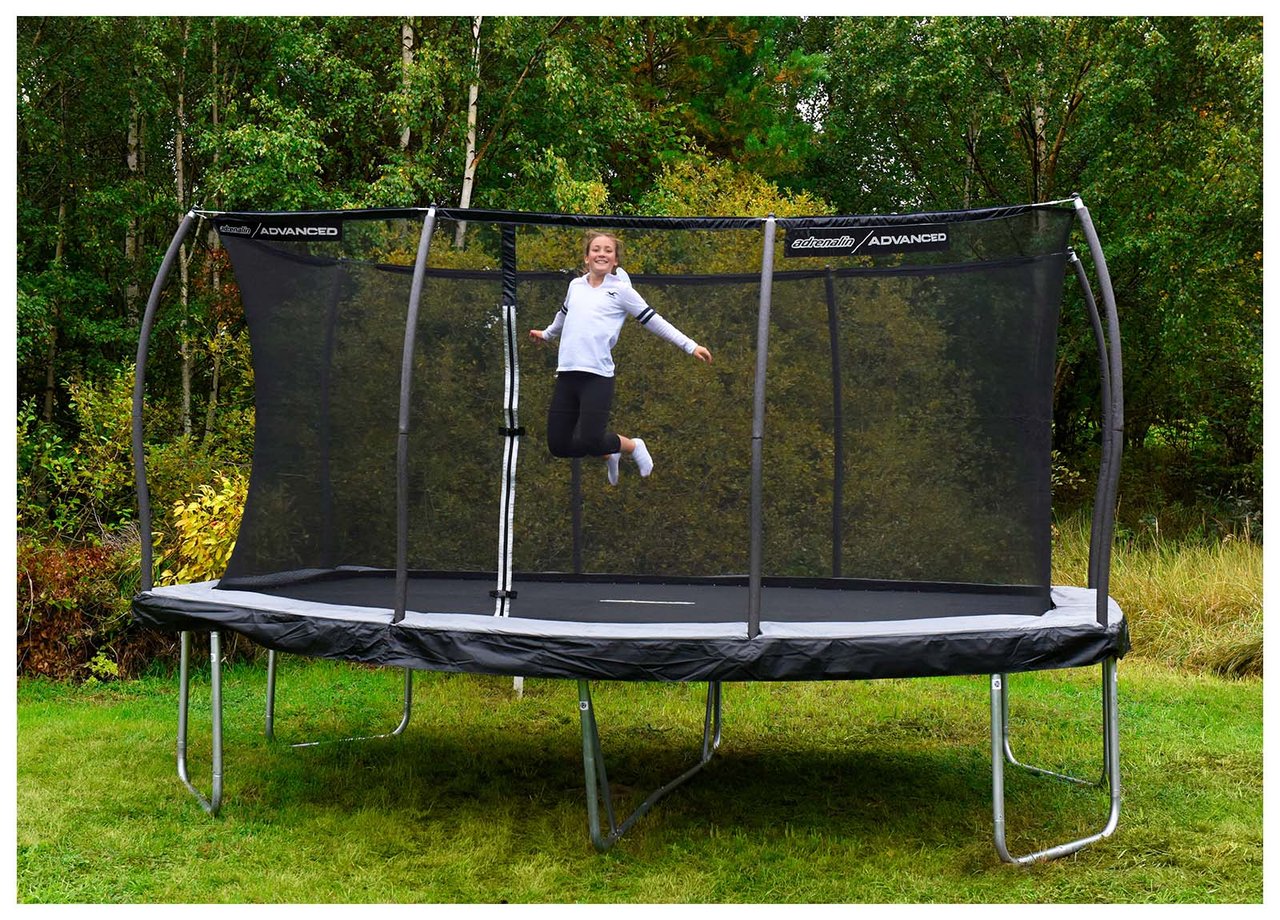 Jente hopper på en stor svart trampoline som står på en gressplen.